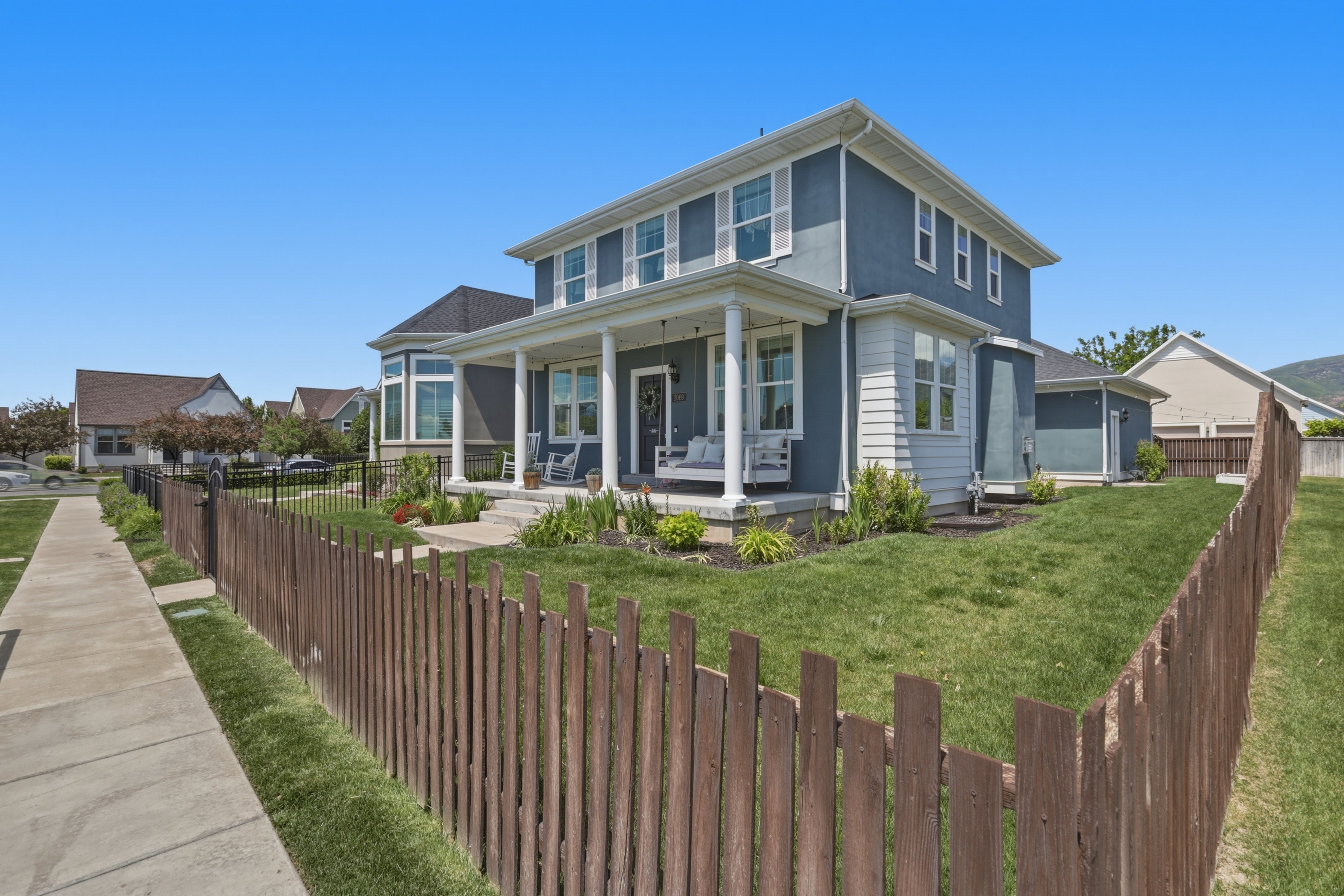 Two-story stucco and siding home with a full-width covered porch, white columns, and perimeter fencing