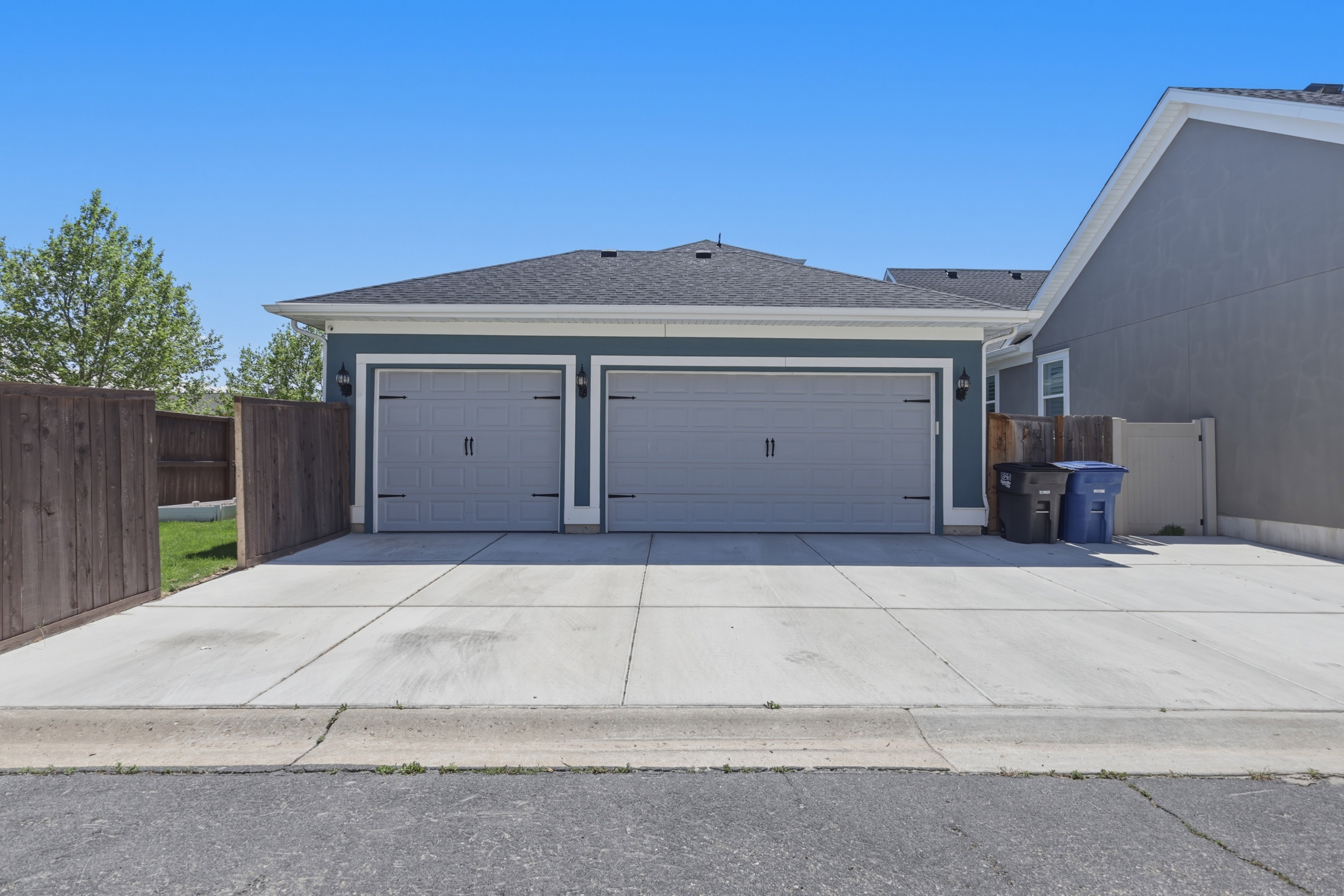 Attached two-car garage featuring a paved driveway, exterior sconce lighting, and a dark shingle roof