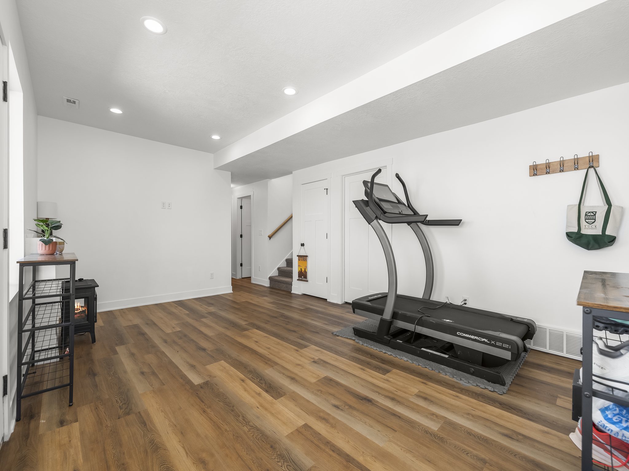 Spacious room featuring wood-finish flooring, recessed lighting, white walls, and a visible staircase with wood handrails