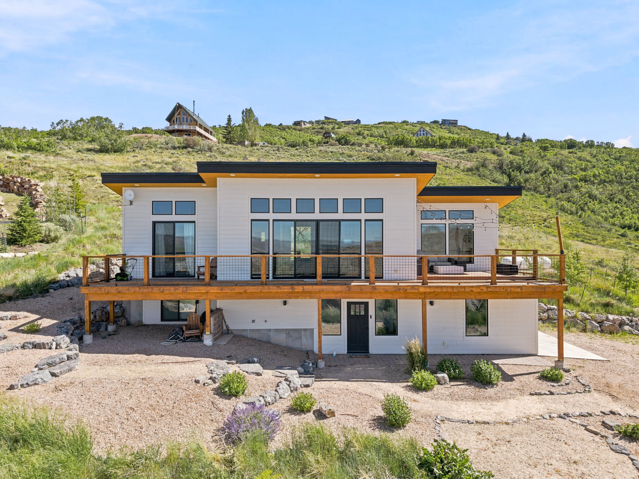 Contemporary residence featuring a spacious wood deck with metal railing, multiple large sliding glass doors, a flat roofline, and a lower-level black entrance door