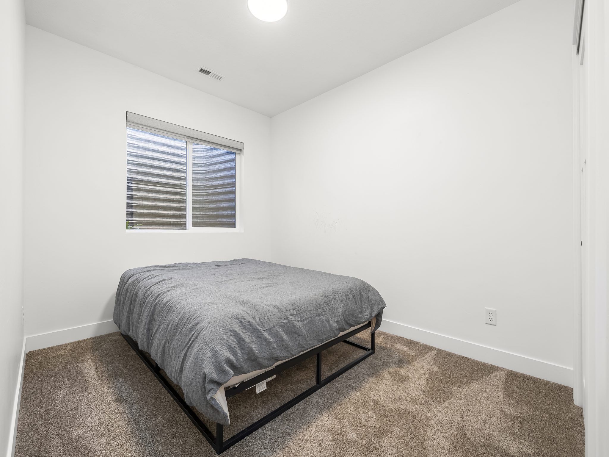 Compact room featuring neutral carpeting, white walls, and a window with blinds