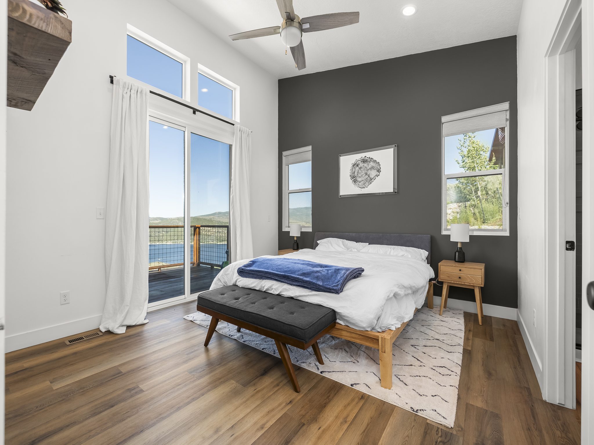 Spacious room featuring vaulted ceilings, wood-finish flooring, a contemporary ceiling fan, and direct access to an outdoor deck through a large glass slider