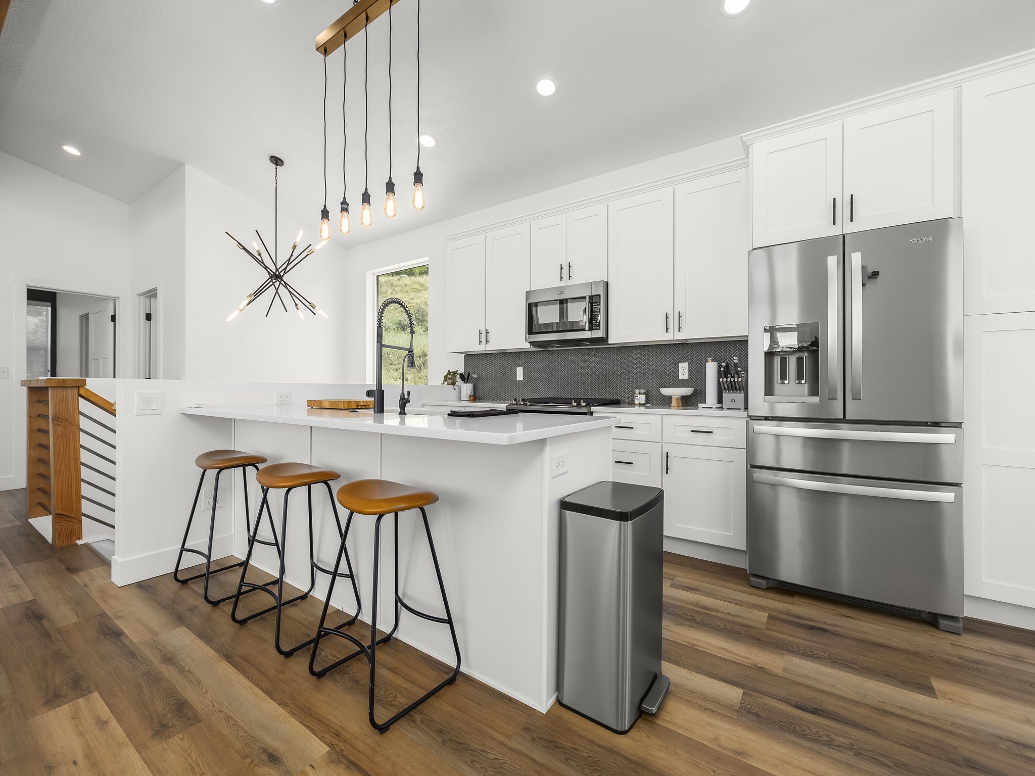 Modern kitchen featuring white shaker cabinetry, stainless steel appliances, a dark mosaic tile backsplash, and wood-finish flooring