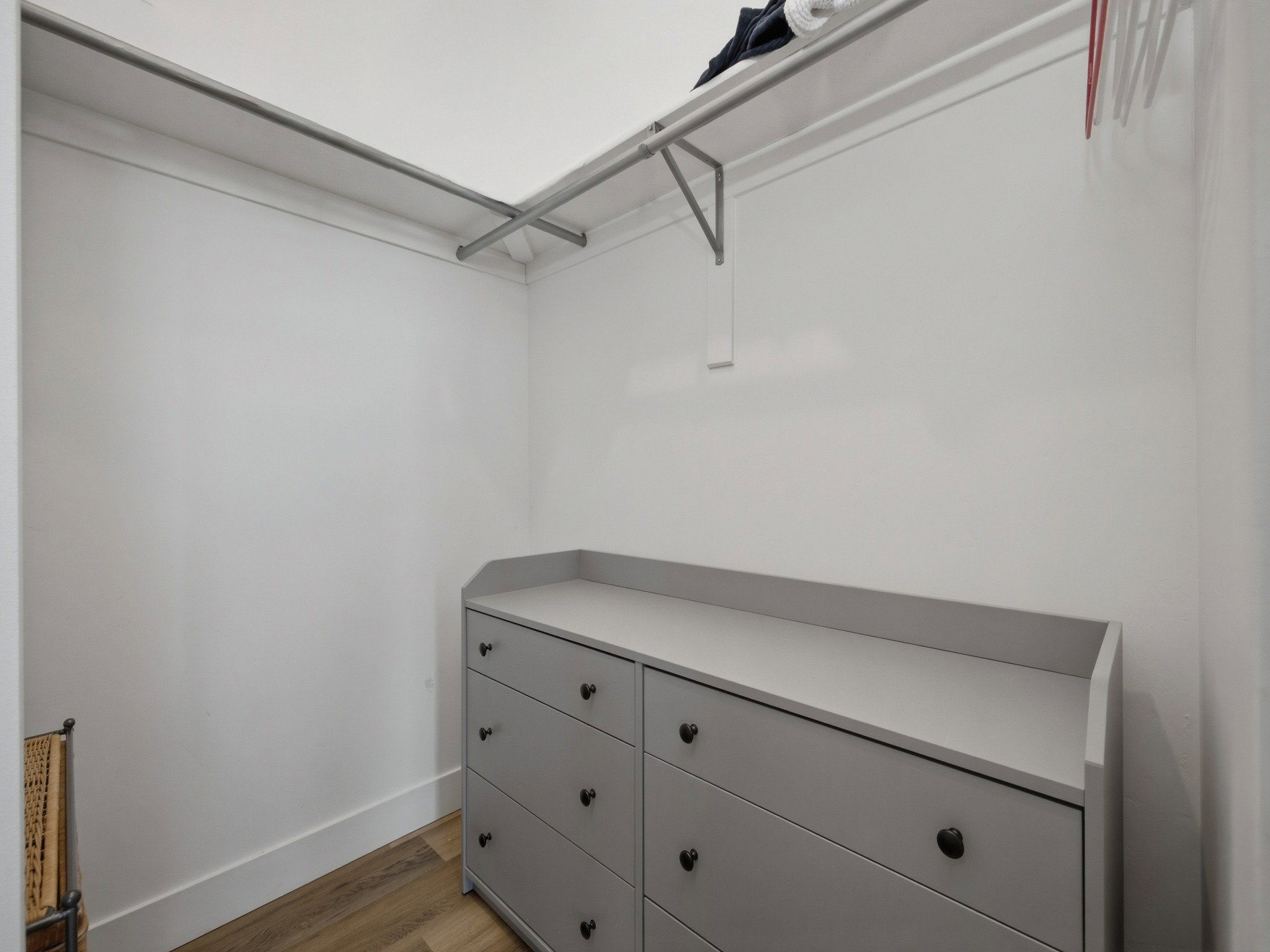 Walk-in closet featuring light wood-finish flooring, white walls, and built-in metal clothing rods