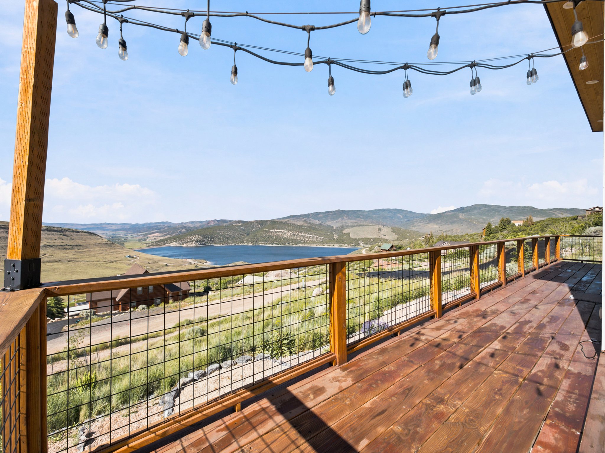 Expansive outdoor deck featuring wood-finish flooring, a wood and wire mesh railing, and string lighting overhead
