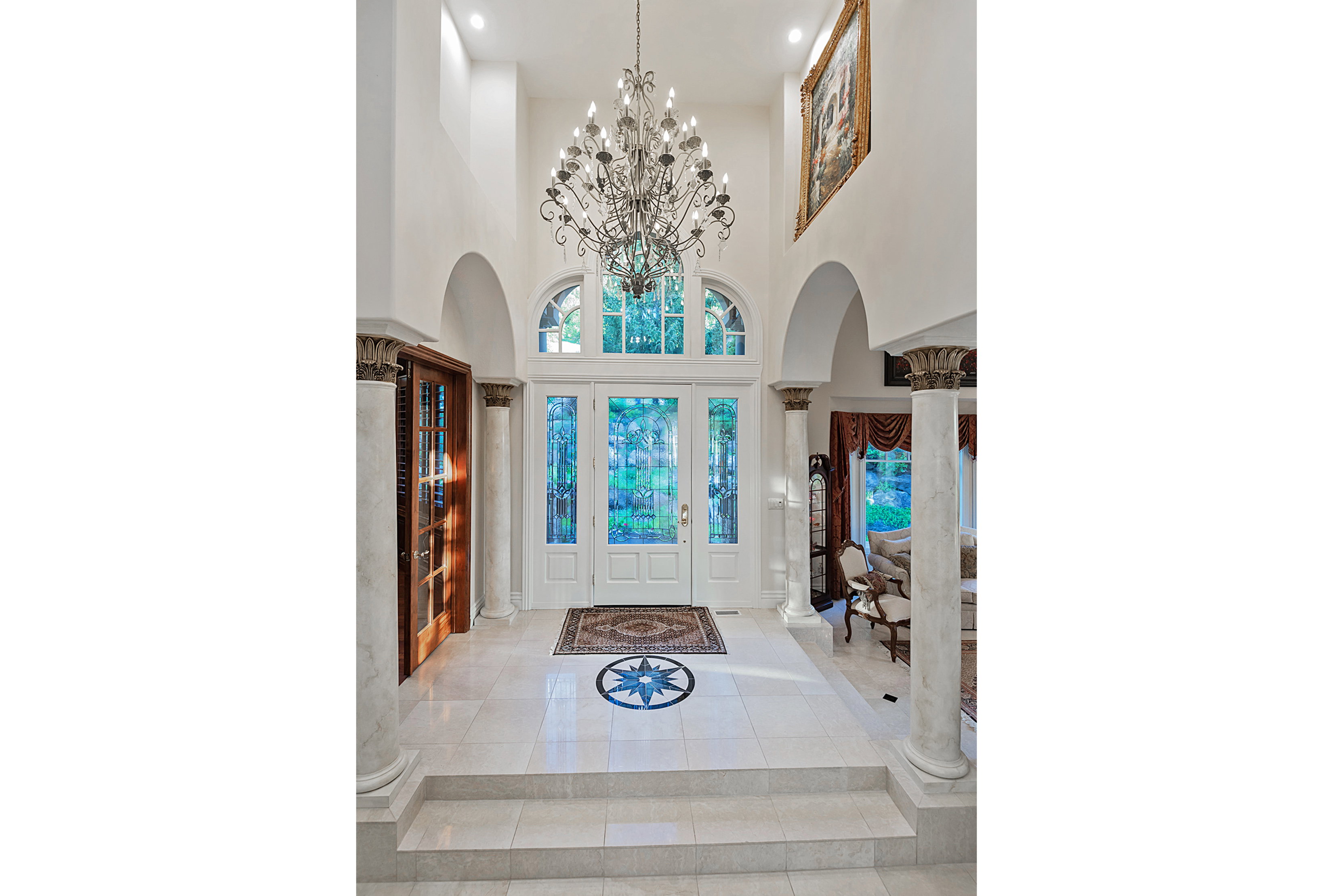 Two-story foyer featuring a grand chandelier, arched doorways, fluted columns, and a custom tile floor medallion