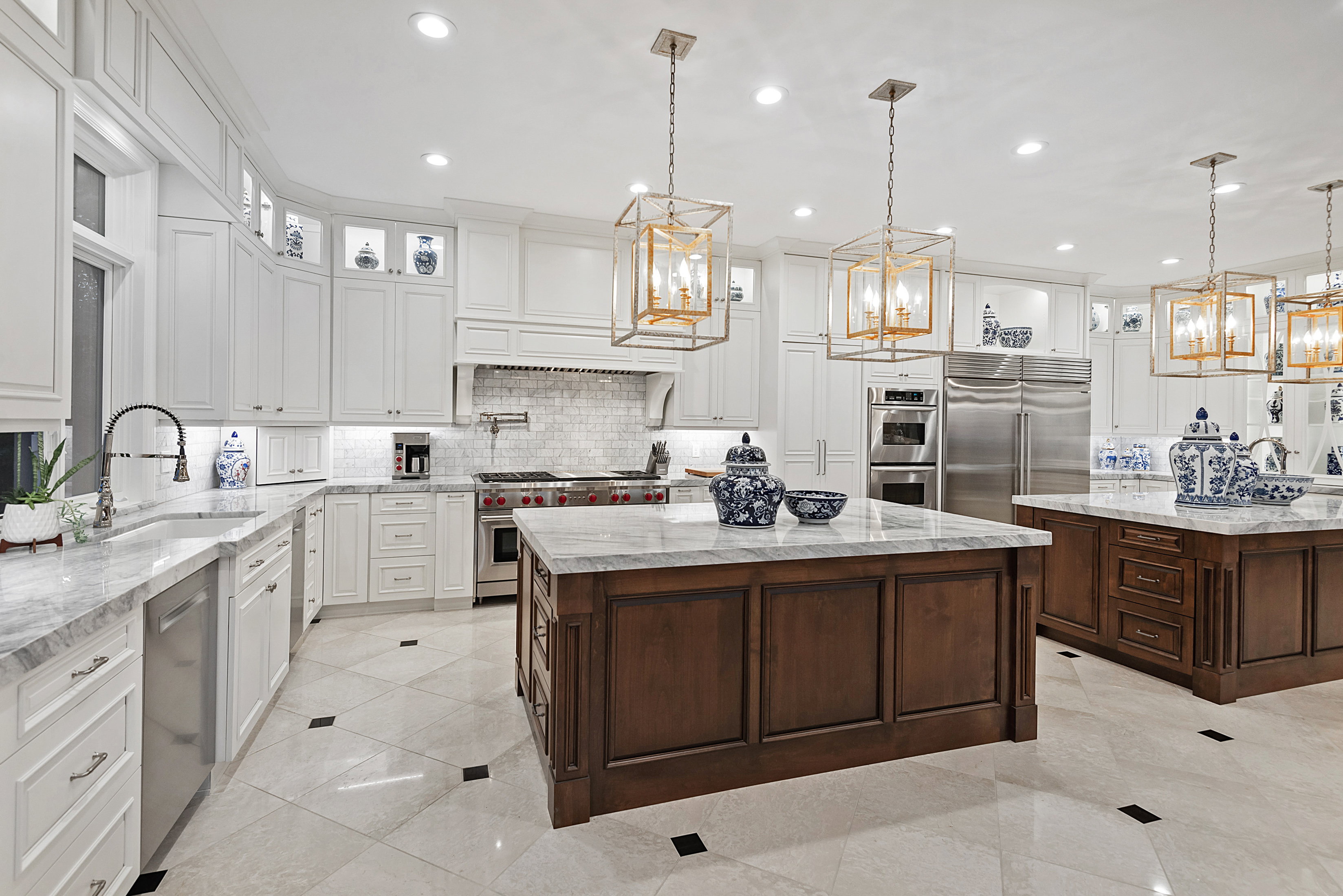 Gourmet kitchen with two wood-paneled islands featuring stone countertops, stainless steel appliances, and white cabinetry