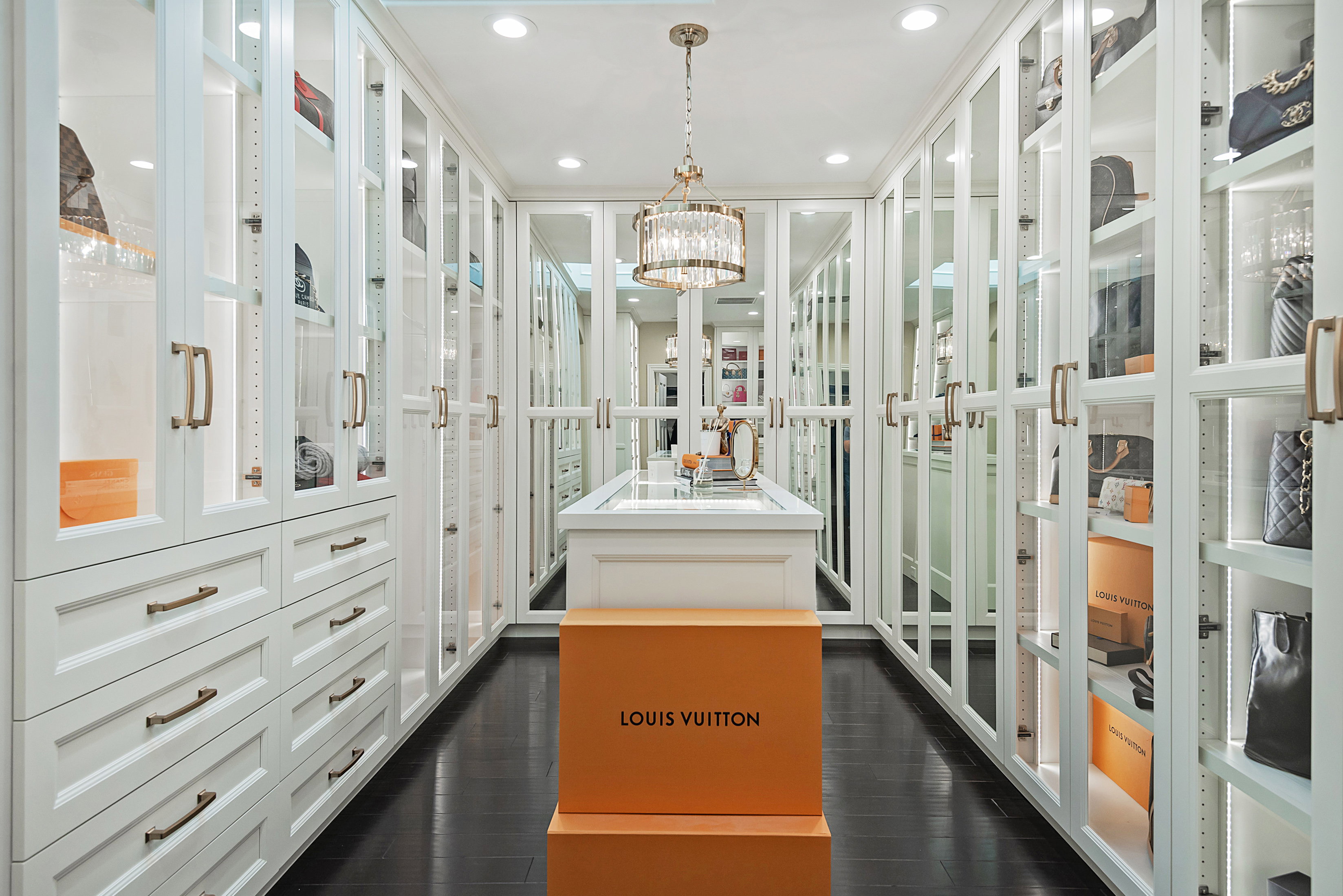 Custom closet featuring extensive built-in cabinetry with glass-front doors, recessed lighting, and a central island with a display top
