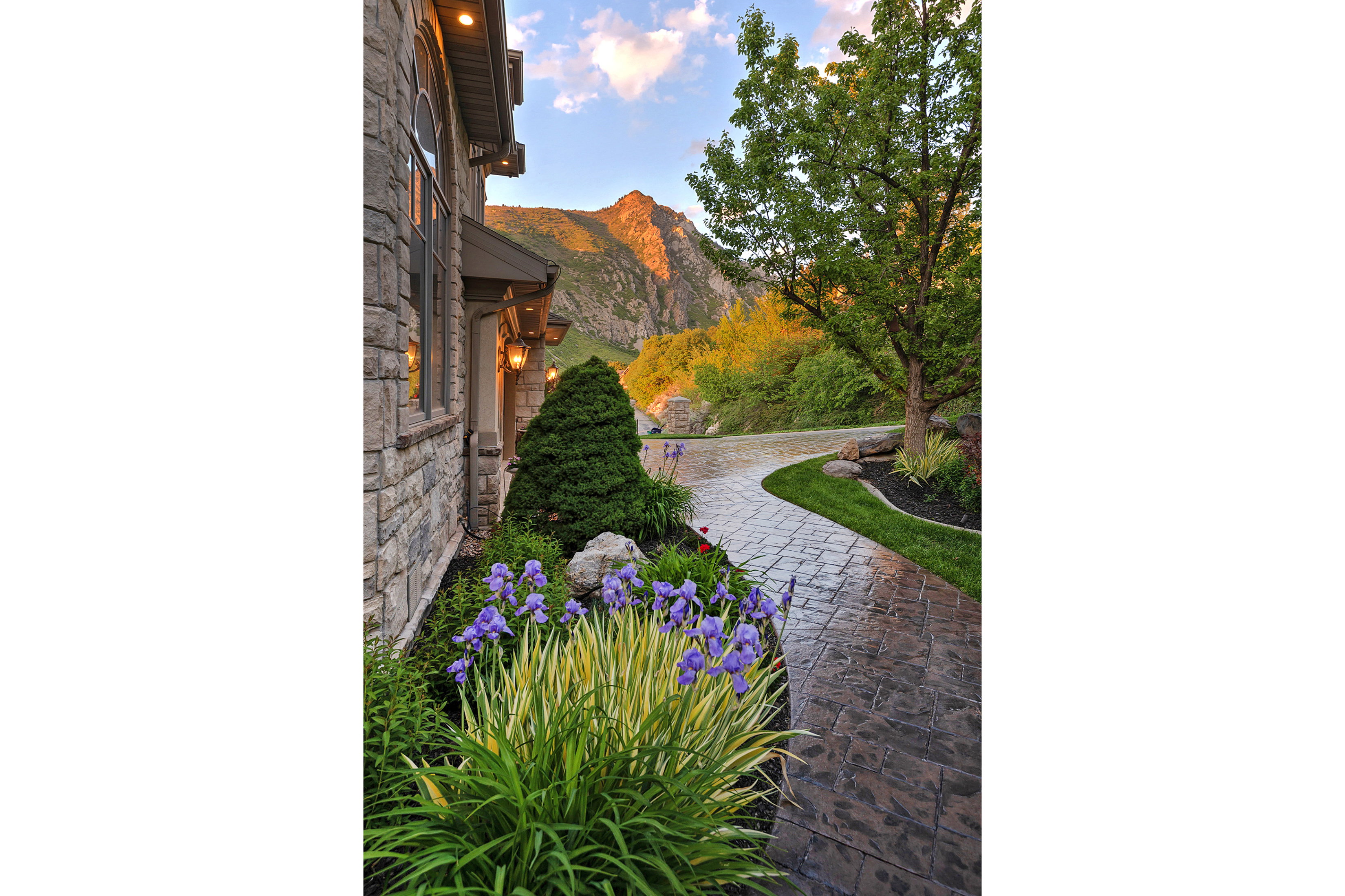 Stone façade with arched window, exterior wall sconces, and a stamped concrete walkway