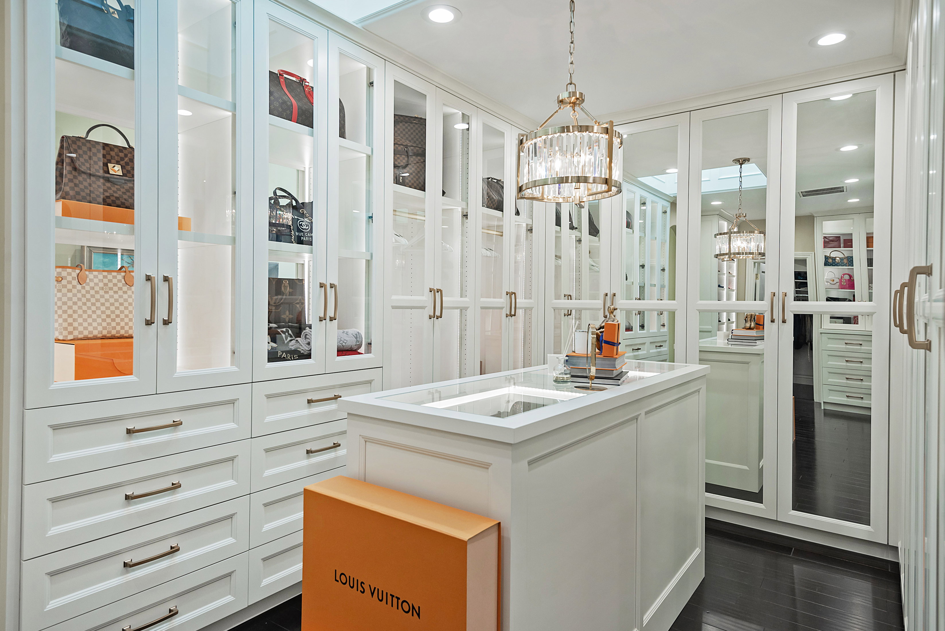 Custom closet system featuring white cabinetry with glass-front display cases and brass hardware
