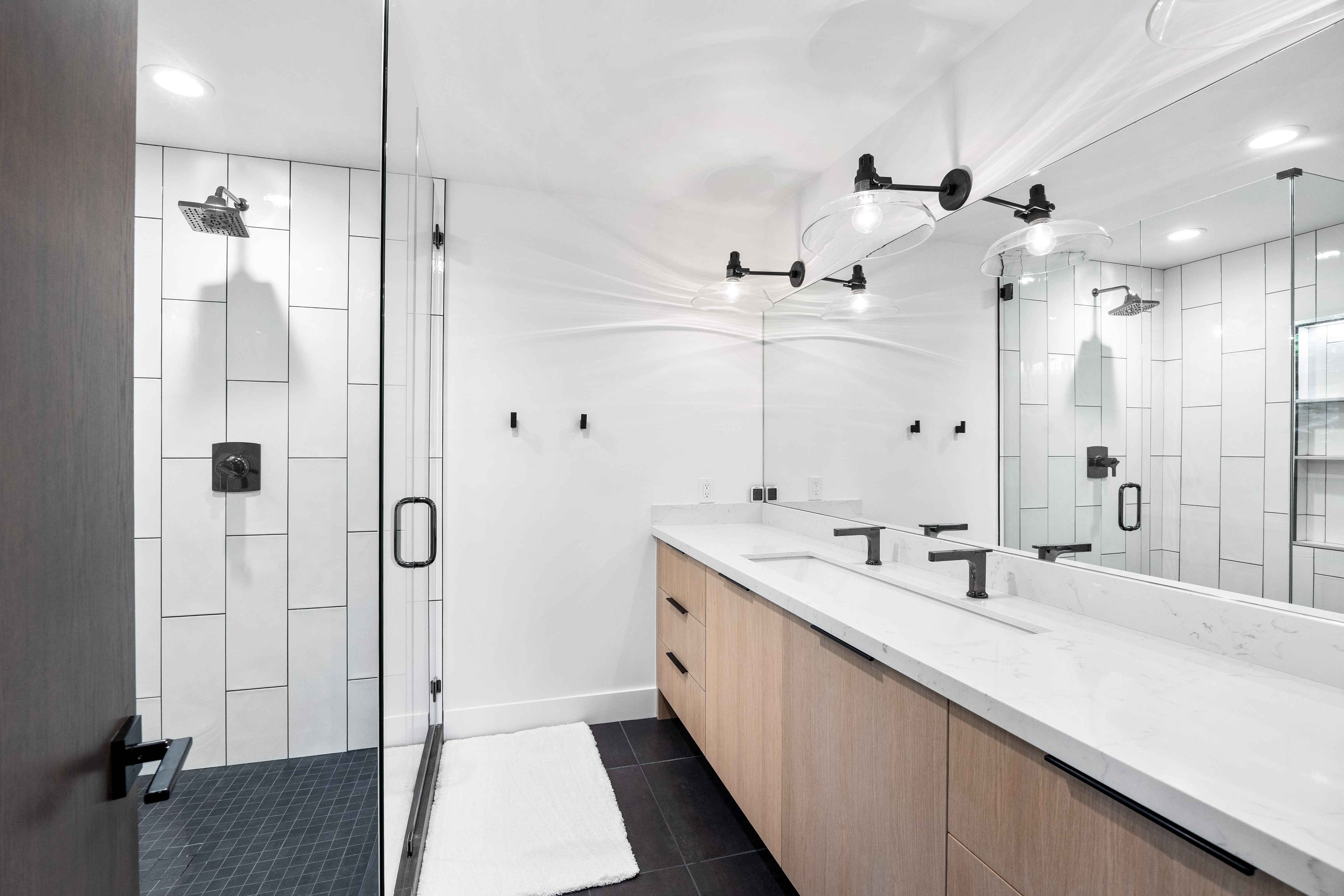 Contemporary bathroom featuring a spacious dual-sink vanity with light wood-finish cabinetry and a white countertop