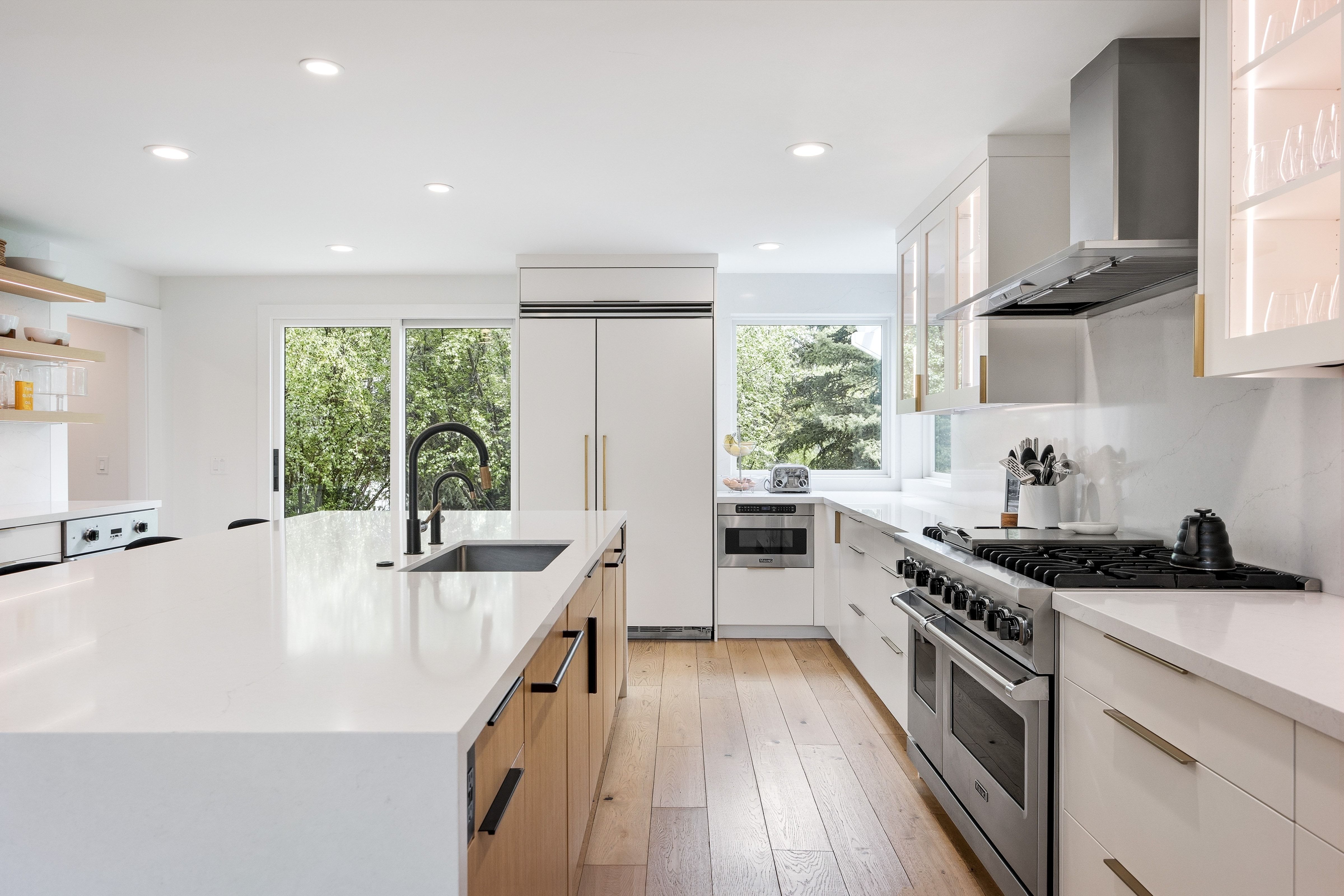 Open-concept kitchen featuring a large island with an undermount sink, stainless steel appliances, wood-finish flooring, recessed lighting, and a sliding glass door