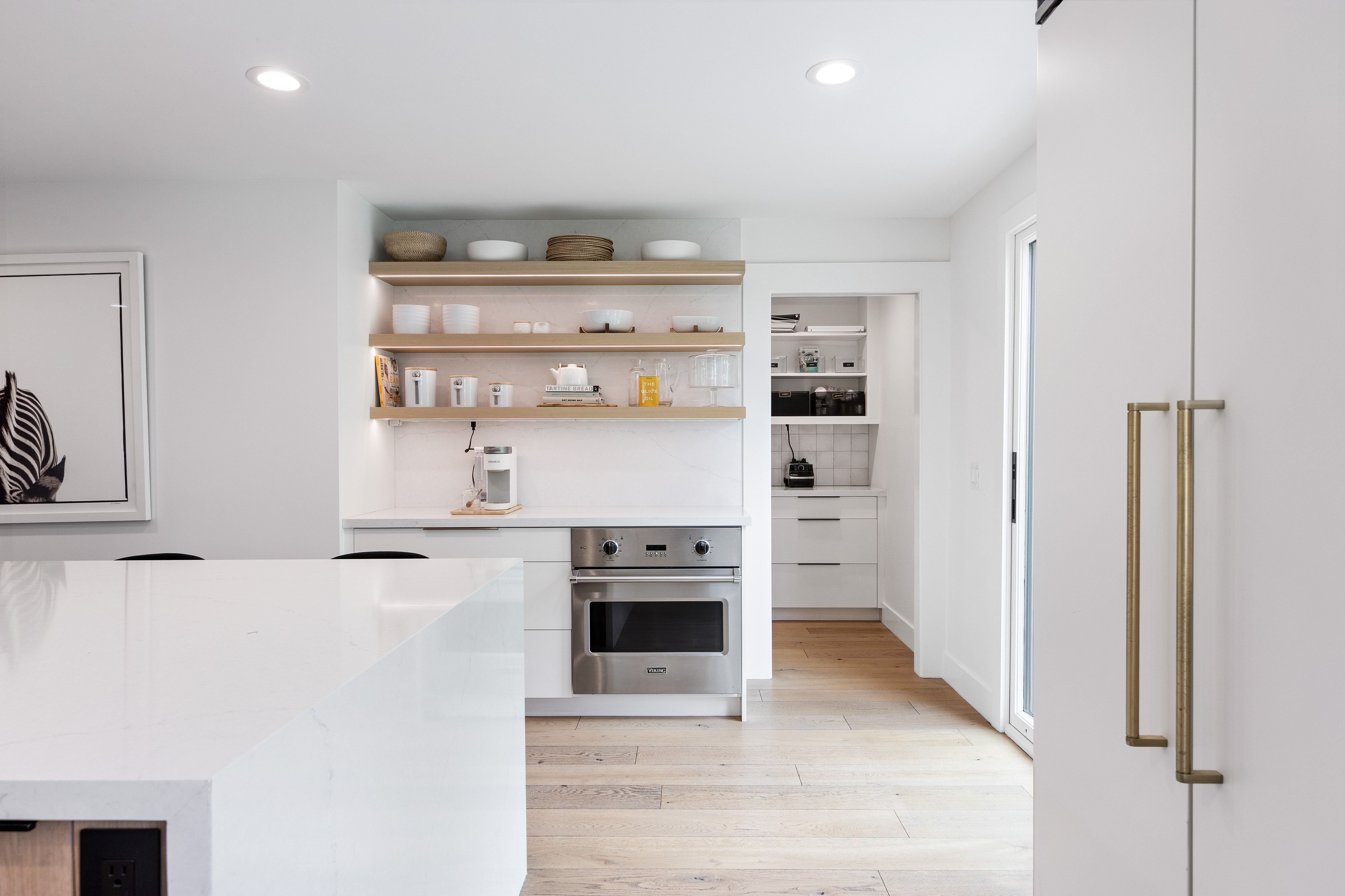 Bright kitchen featuring a white countertop island, stainless steel built-in oven, light wood-finish flooring, and open shelving