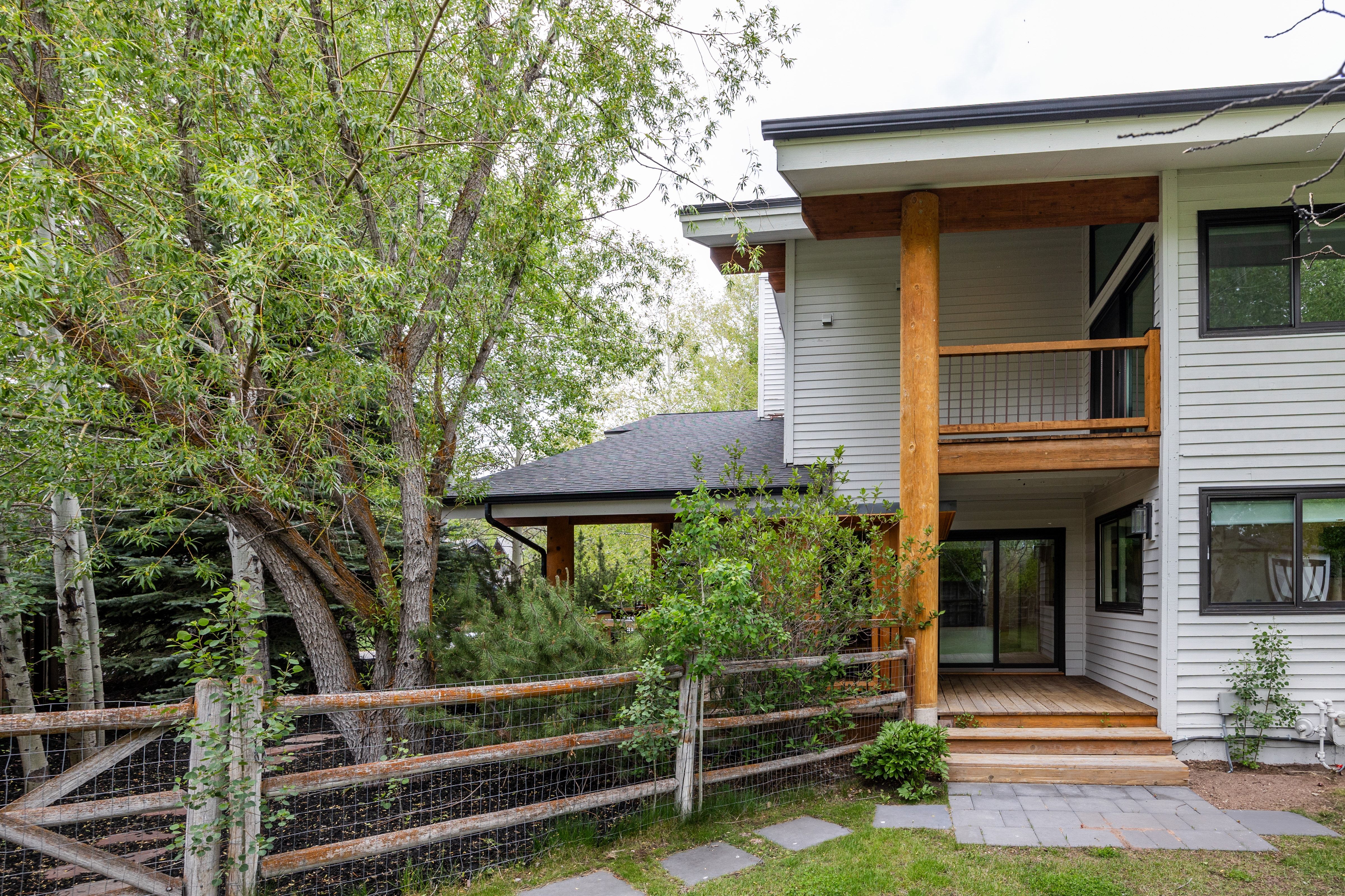 Contemporary exterior featuring light-colored siding, a second-story balcony with wood railing, a ground-level wood deck, black-framed windows, and stone pavers leading to the entrance