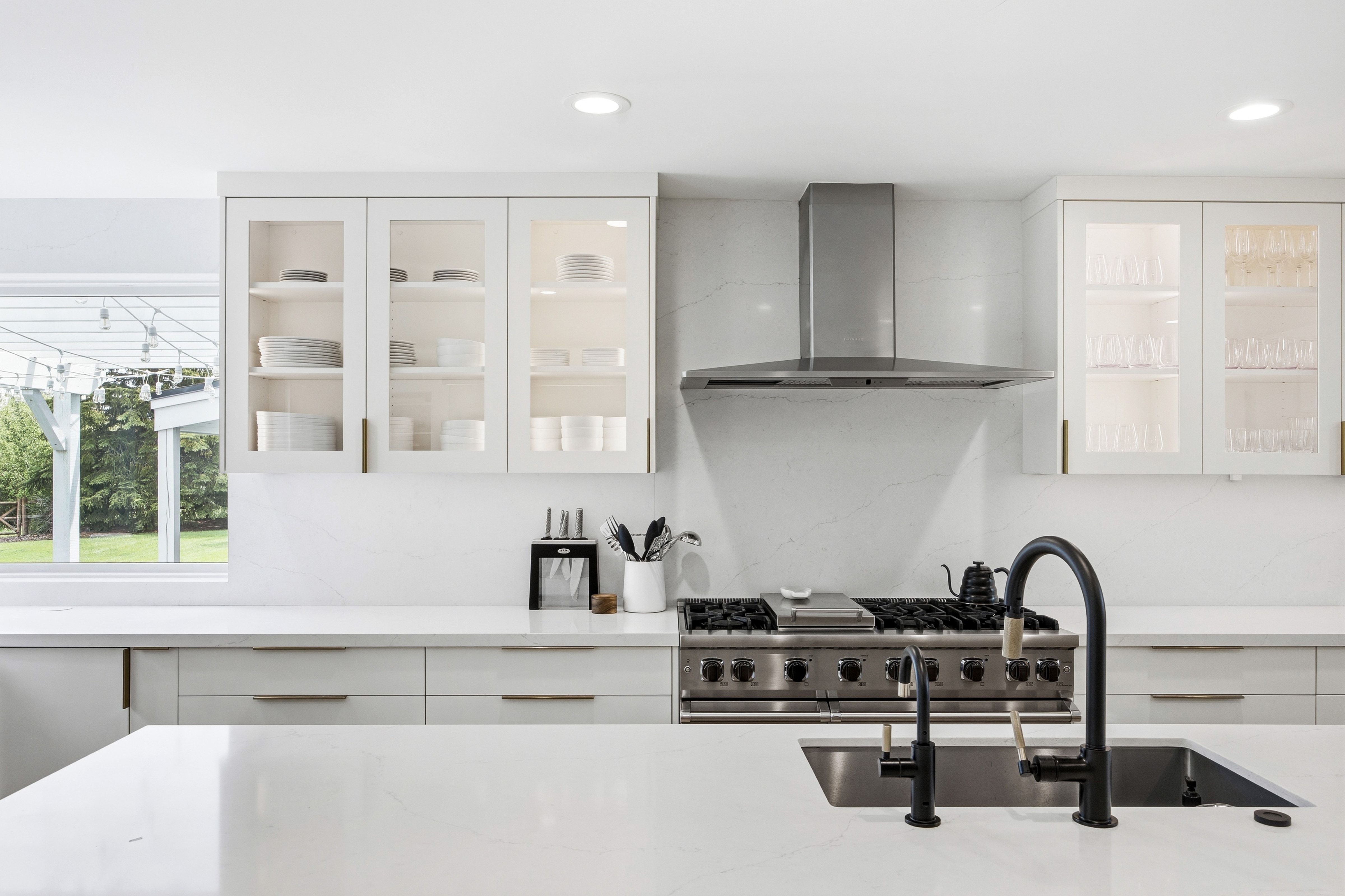 Kitchen featuring a stainless steel range with a professional-grade hood, white quartz countertops, and a large sink with a matte black faucet