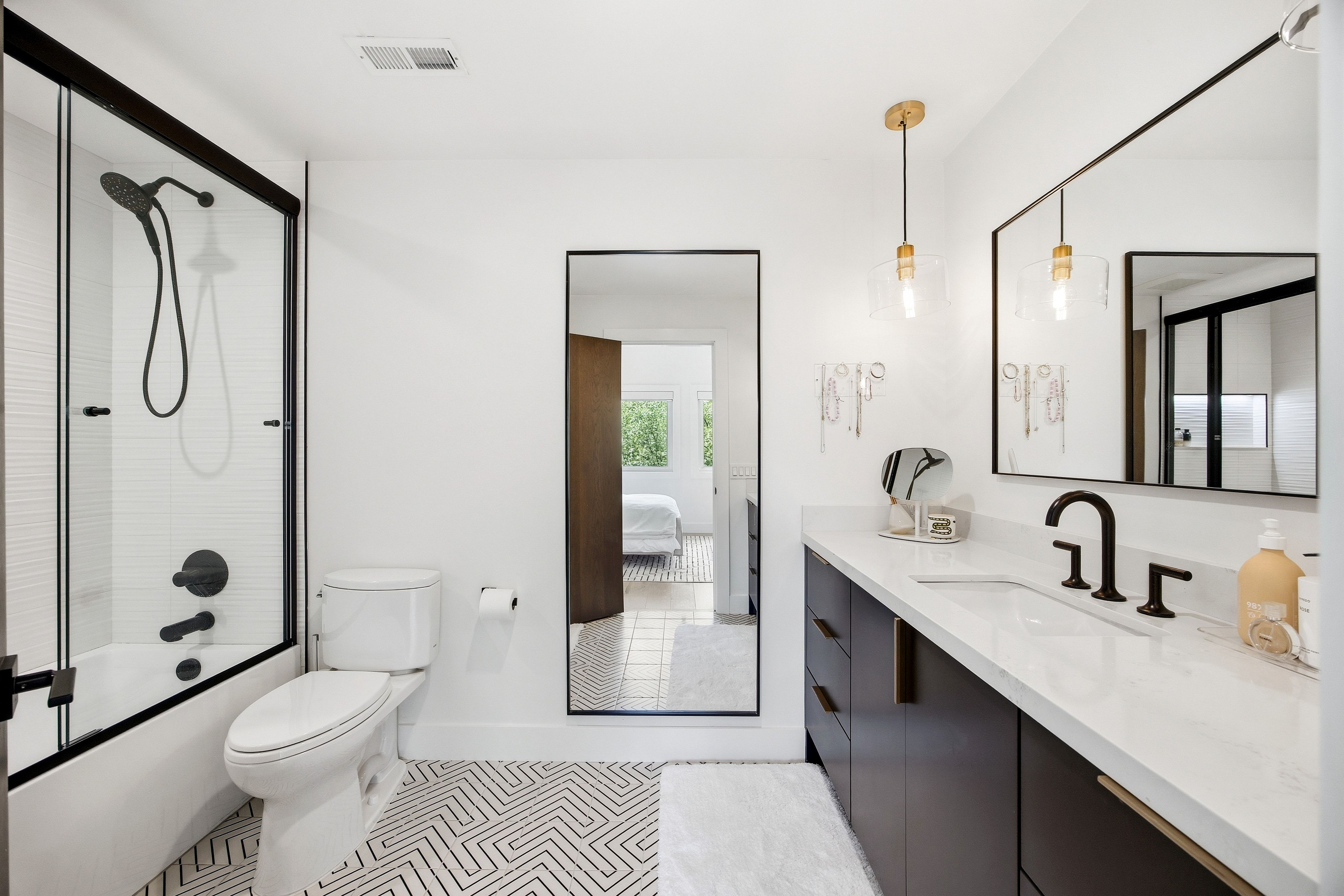 Modern bathroom featuring a single vanity with a white countertop and dark cabinetry, a spacious mirror, and matte black fixtures