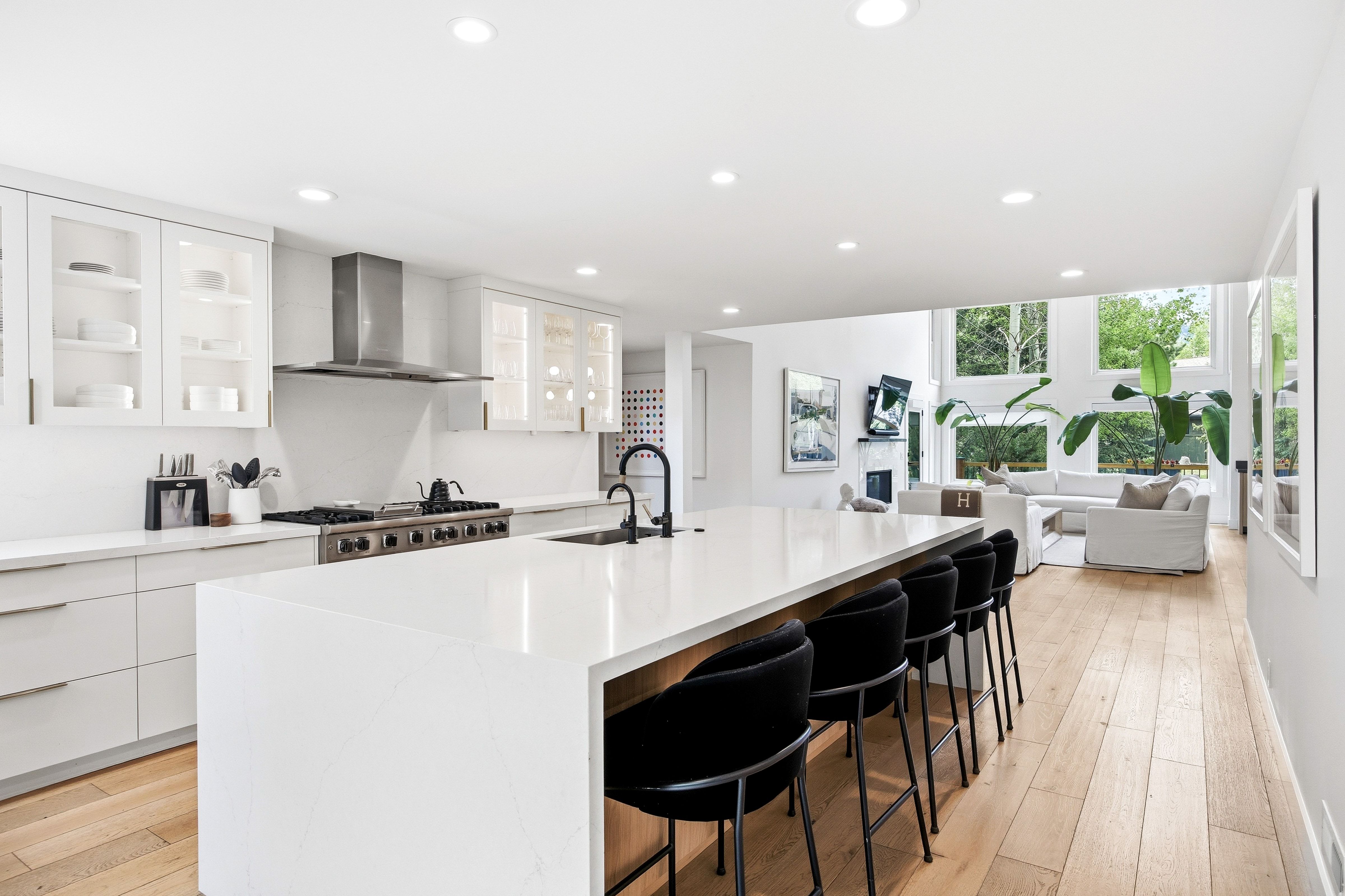 Open-concept kitchen featuring a large island with seating, stainless steel appliances, white cabinetry, and wood-finish flooring