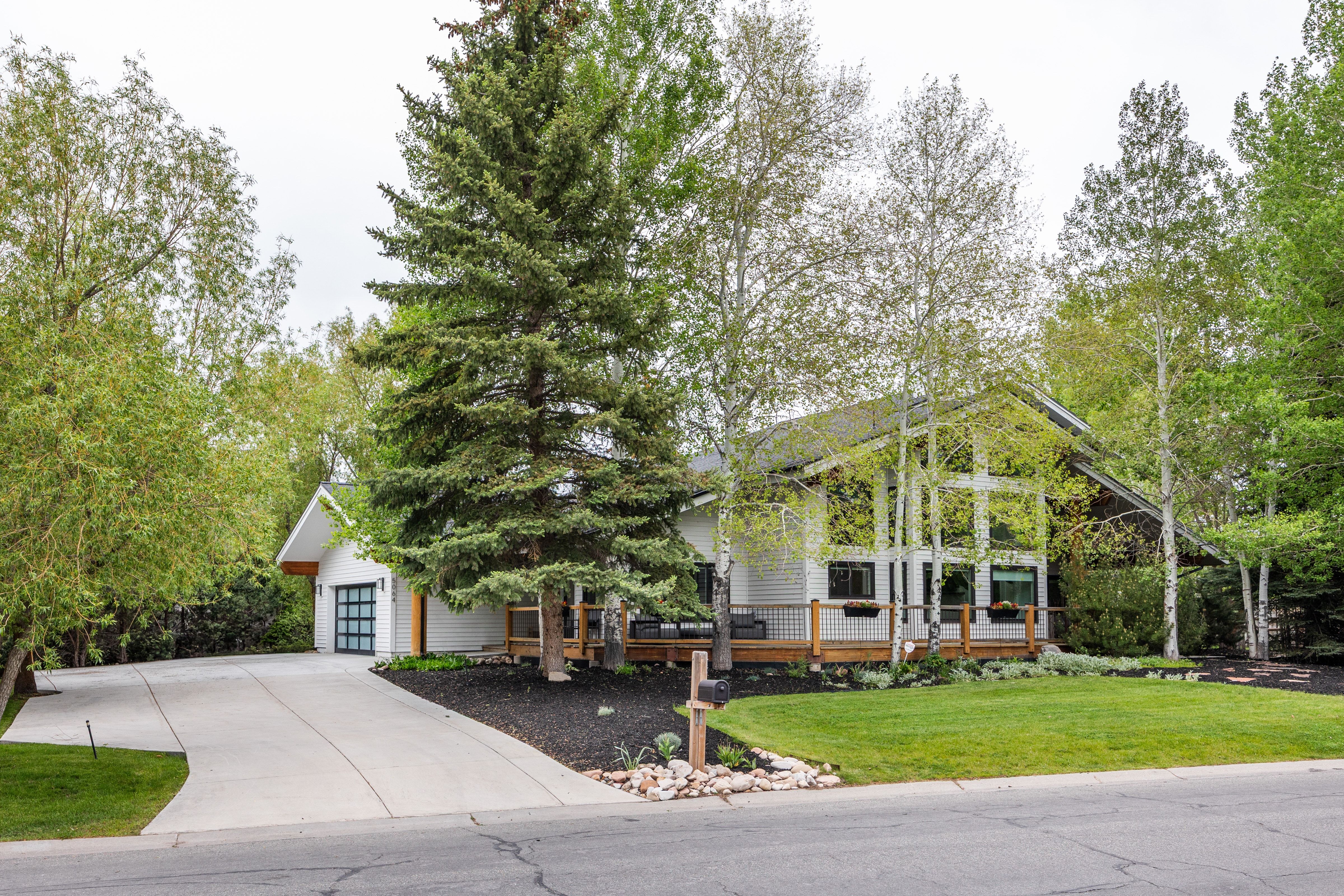 Contemporary architectural style featuring a prominent glass façade, expansive front deck, attached garage with a modern glass door, and a concrete driveway