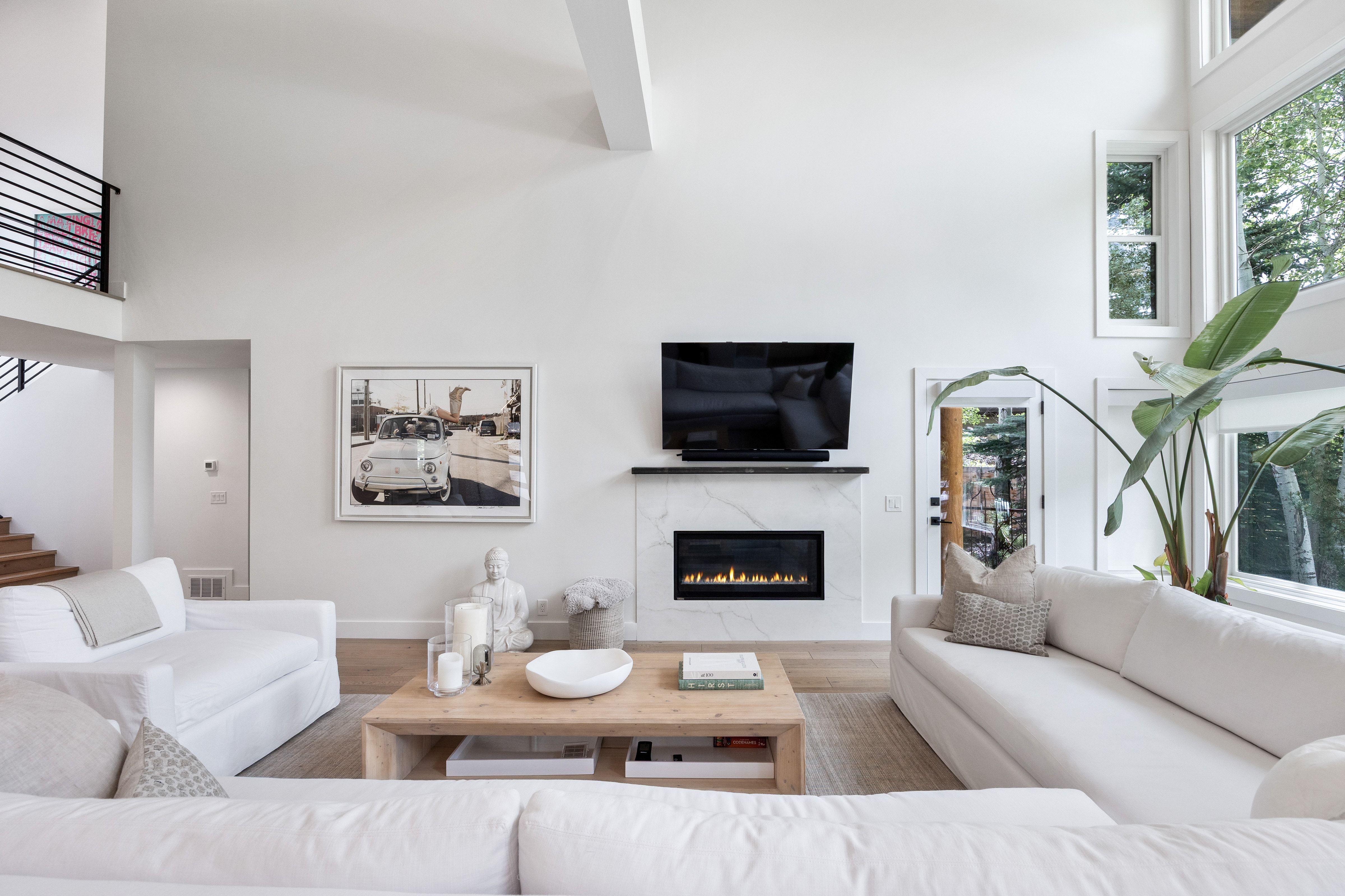 Vaulted living space featuring a modern fireplace with a light-toned surround, hardwood flooring, and abundant natural light from large windows