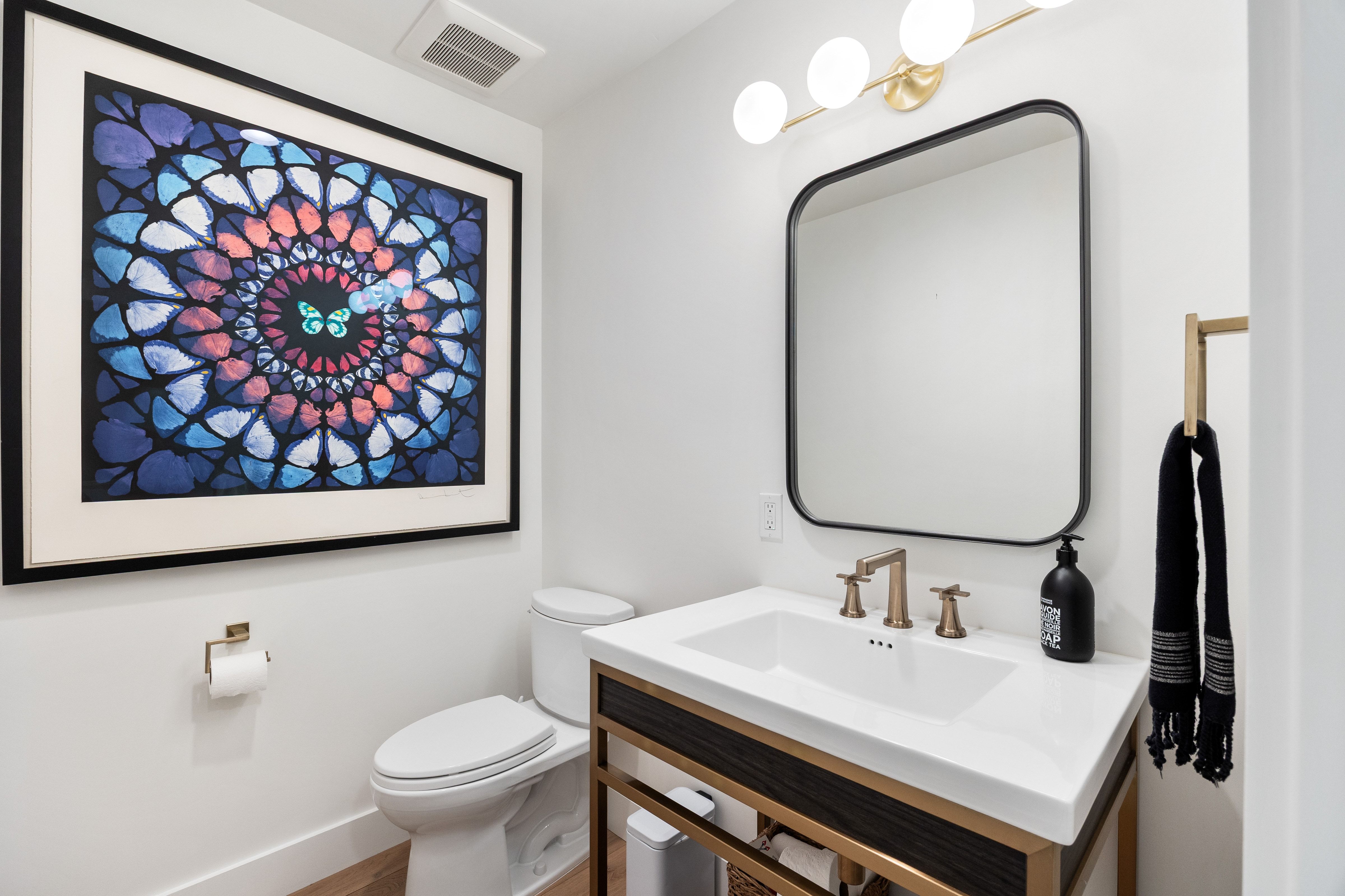 White vanity with an integrated rectangular sink and bronze-finish faucet, framed by a matte black mirror and overhead globe lighting