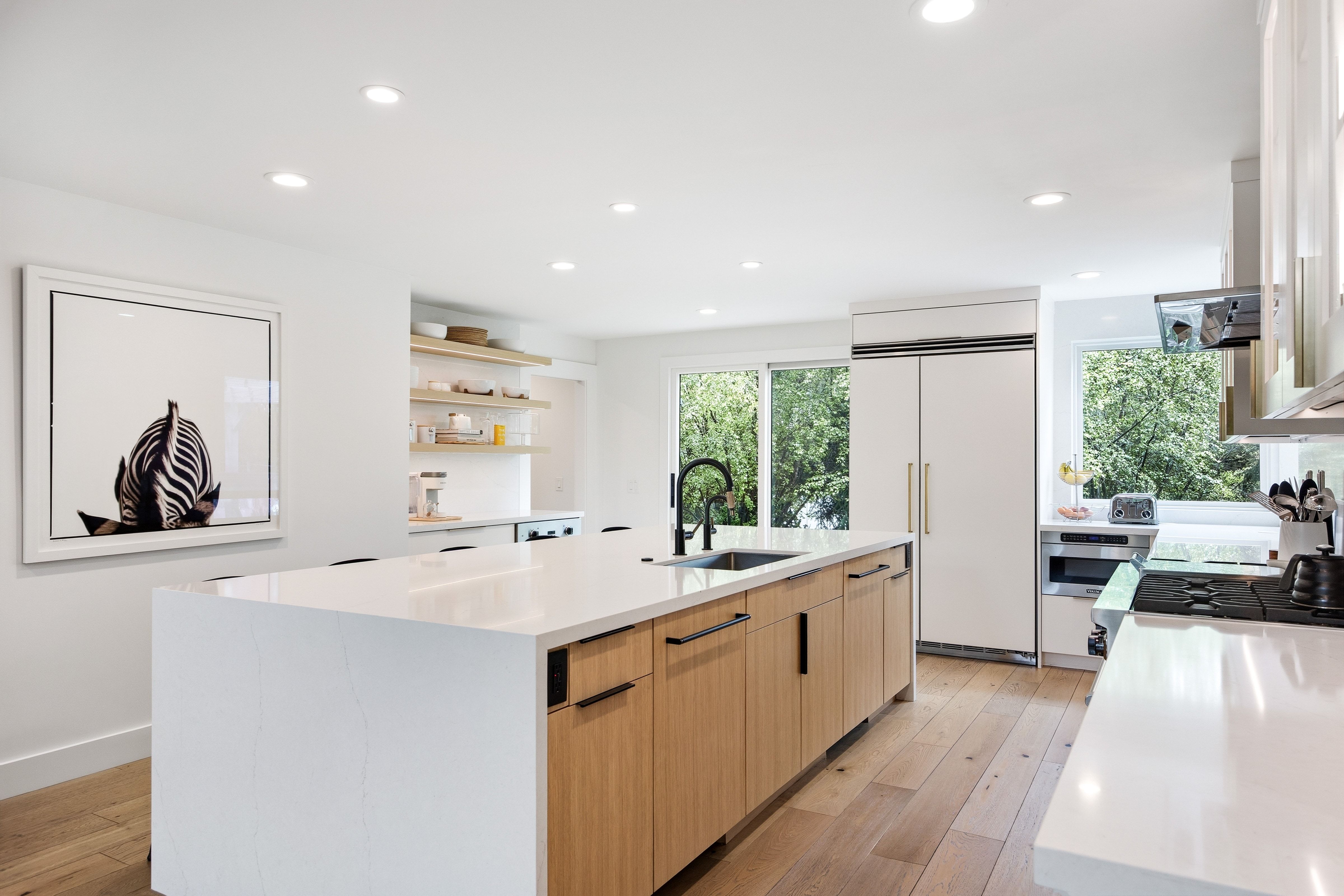 Bright kitchen featuring a substantial island with integrated sink, light wood-finish cabinetry, and white countertops