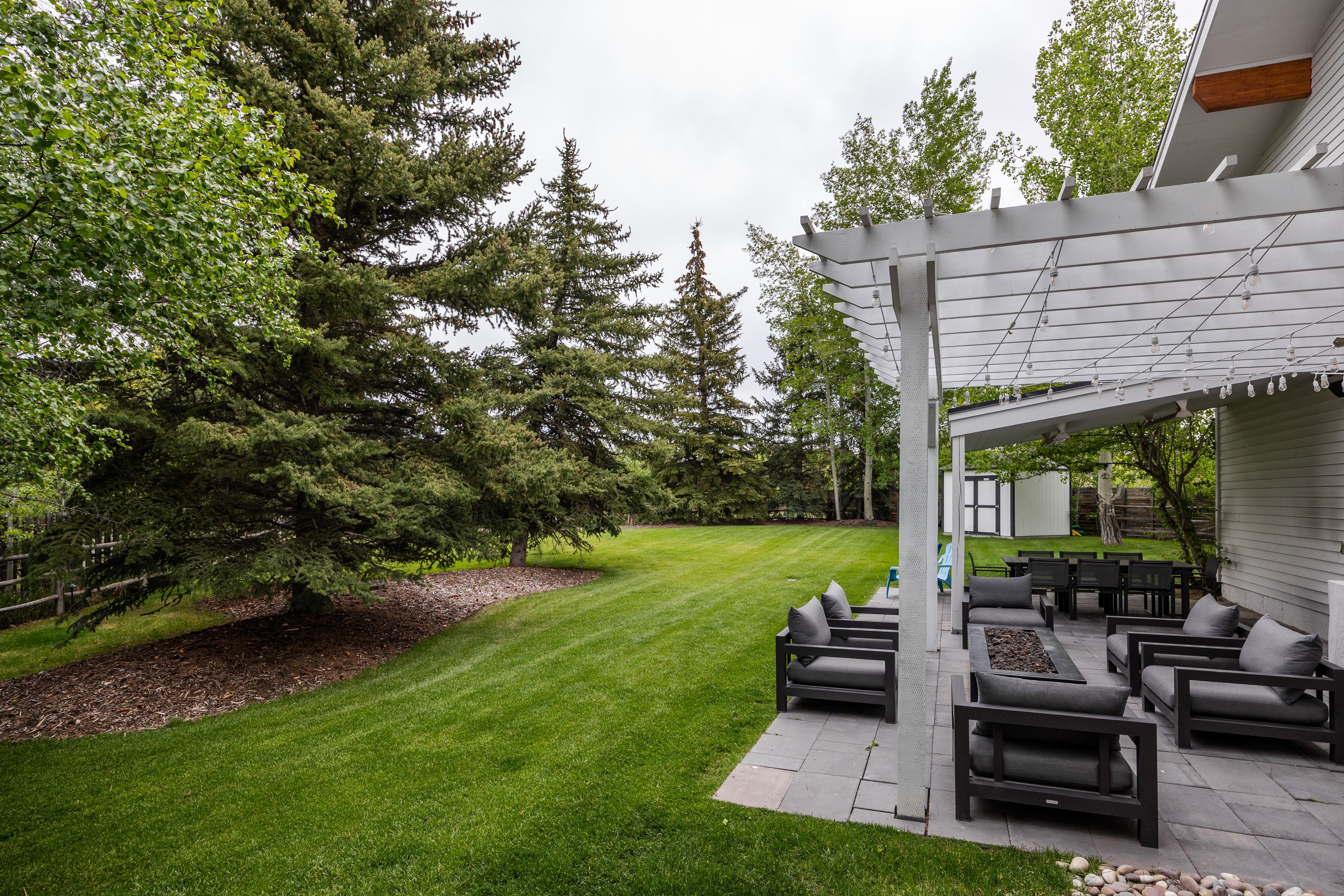 Expansive backyard featuring a large paved patio with a pergola, a stone fire pit, and a spacious lawn