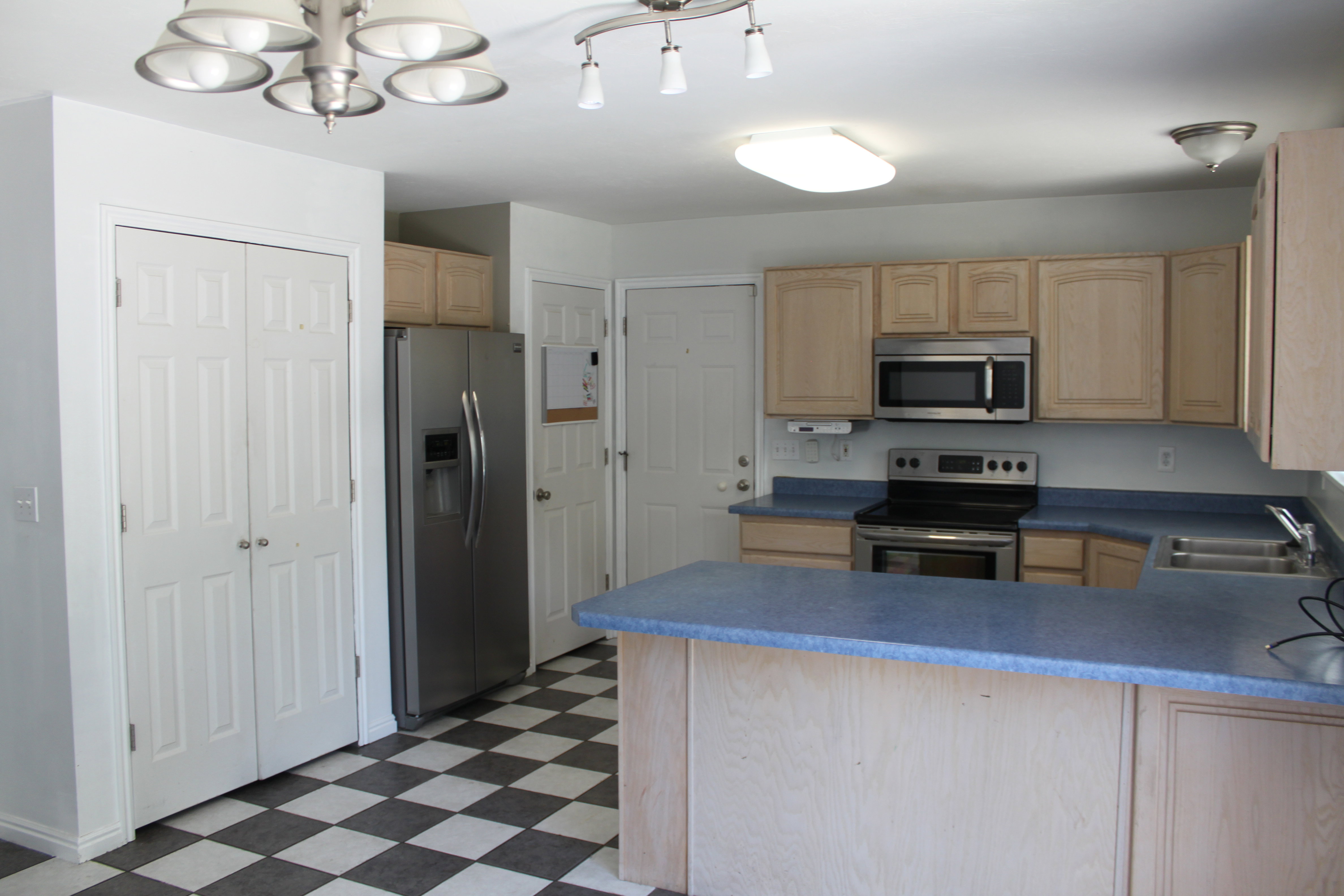 Kitchen featuring light wood cabinetry, stainless steel appliances, blue countertops, and checkerboard floor tiles