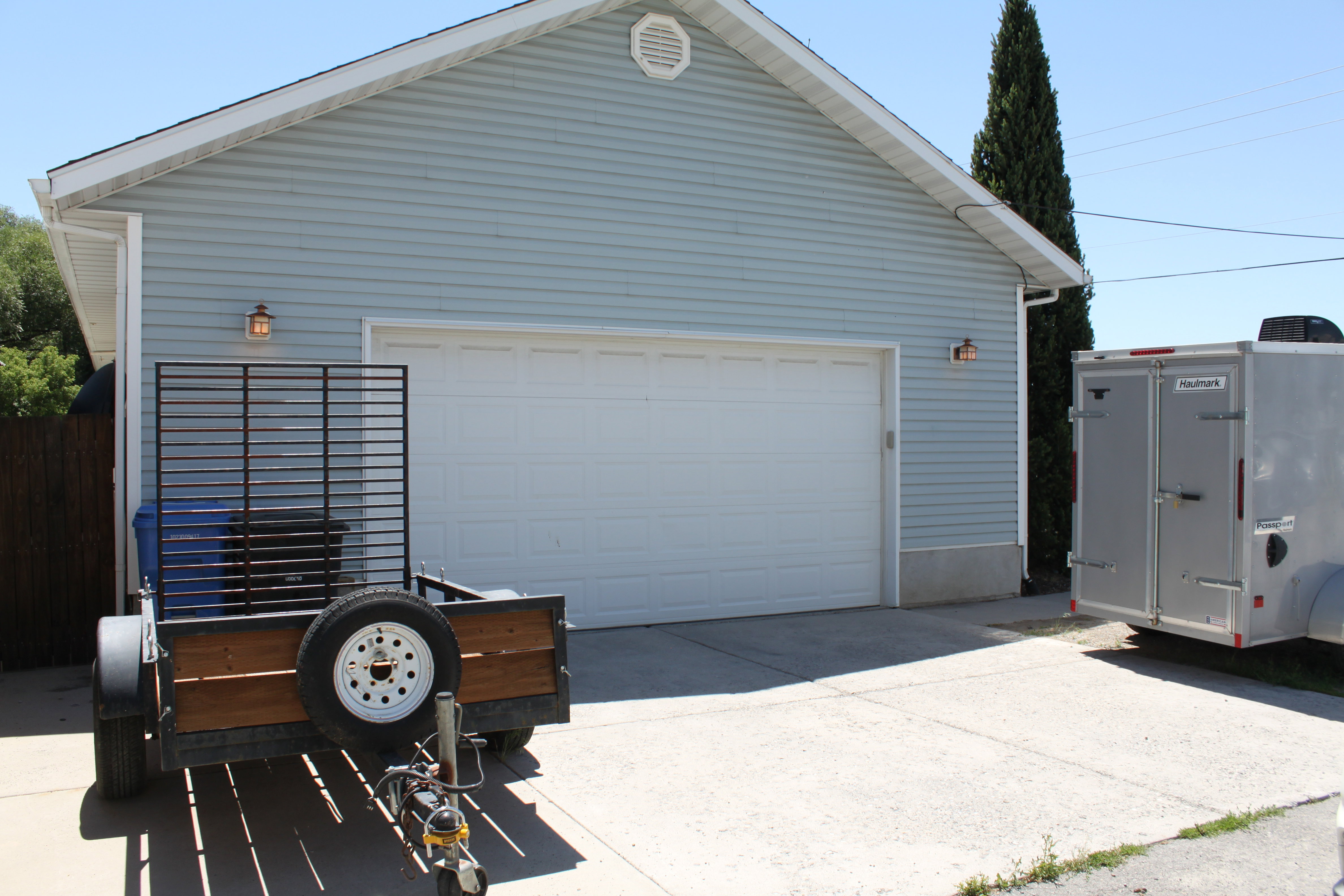 Light blue vinyl siding garage featuring a white overhead door and two exterior light fixtures