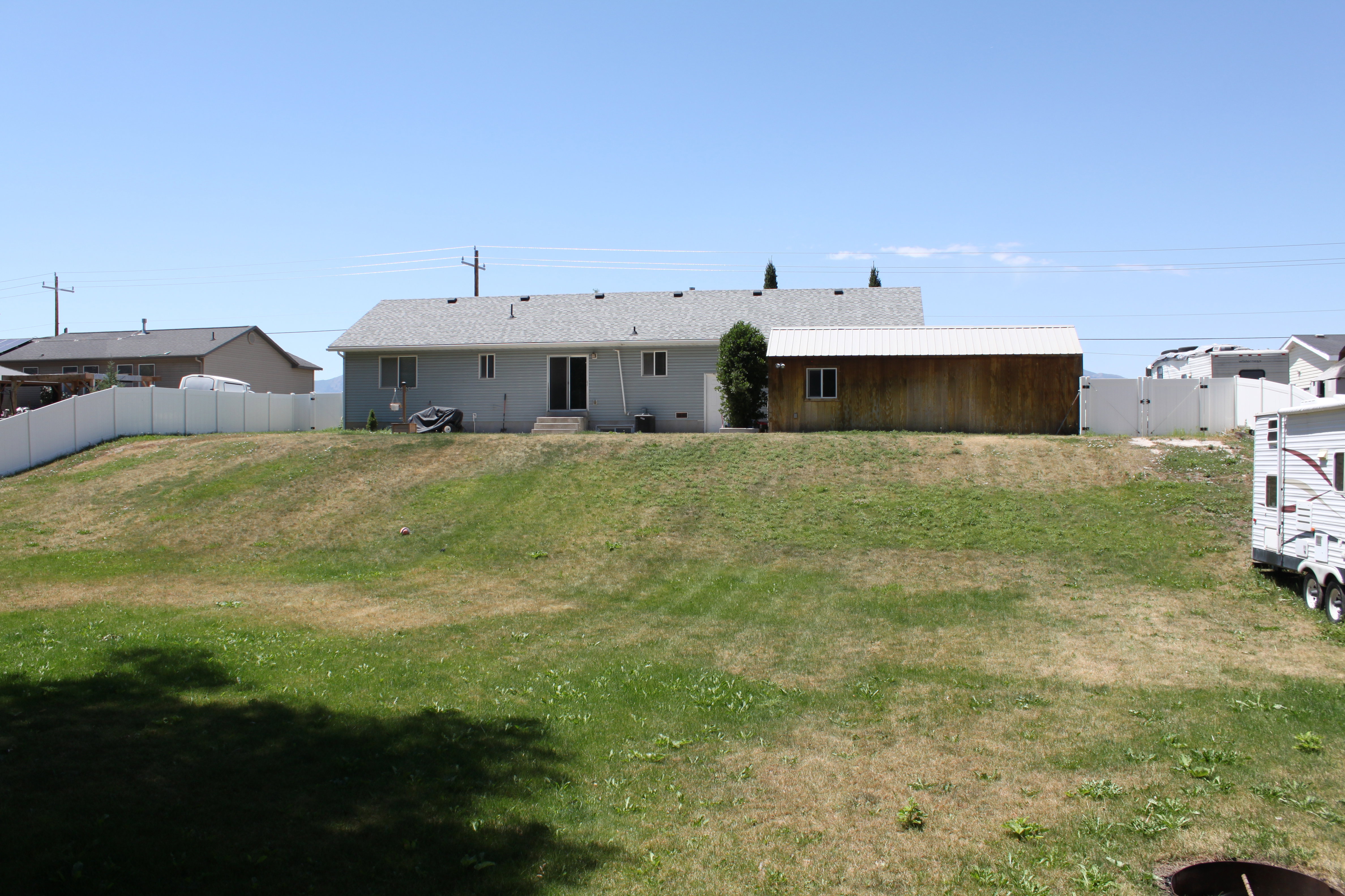 Expansive backyard featuring a sloped lawn and a white vinyl privacy fence