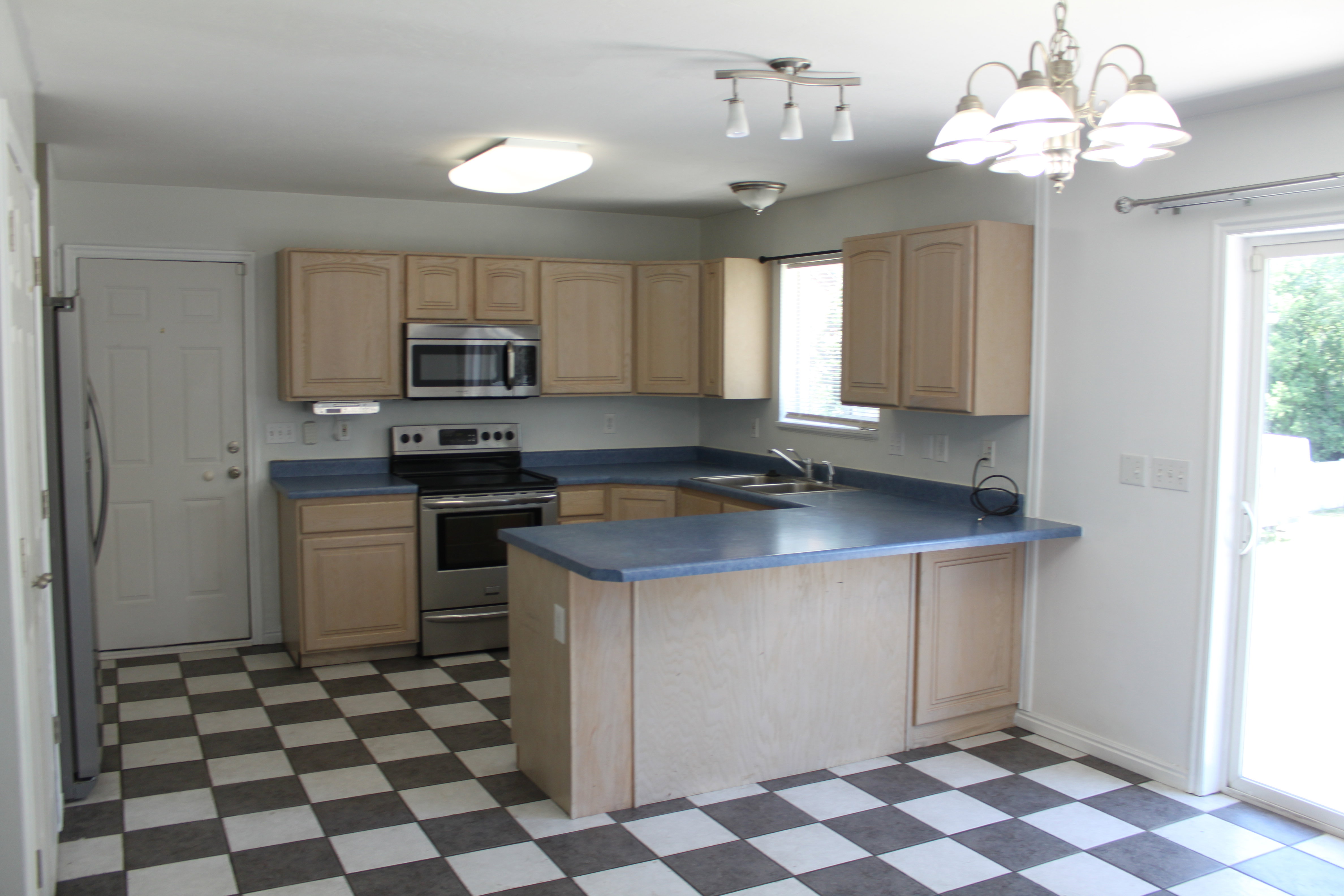 Kitchen featuring checkerboard flooring, light wood-finish cabinetry, blue countertops, and stainless steel appliances