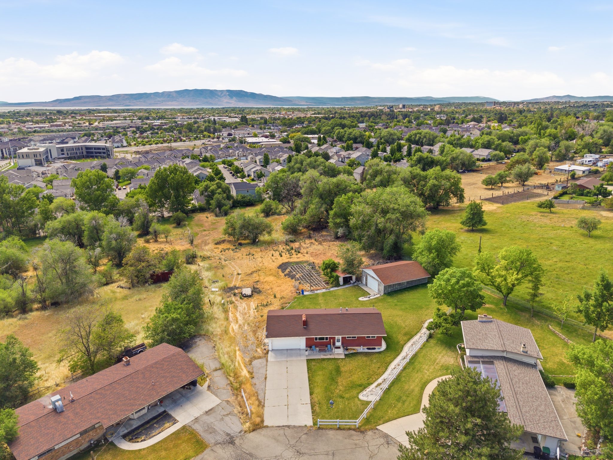 Aerial perspective showcasing a red-sided residence with a brown shingle roof and an attached concrete driveway