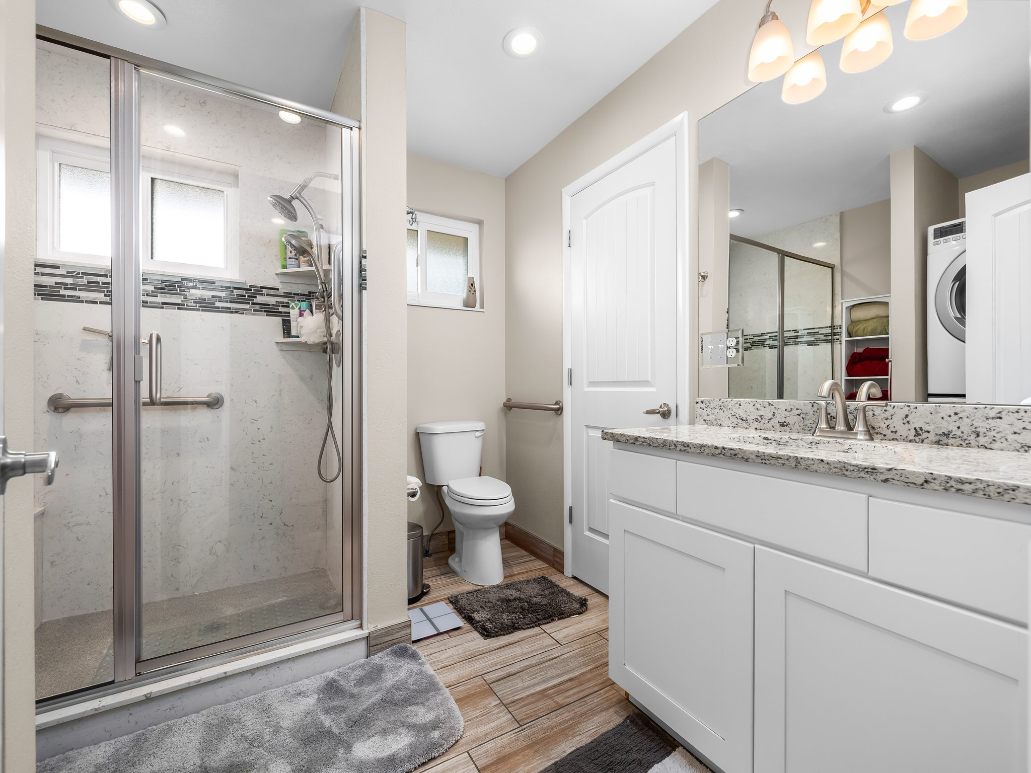 Bathroom featuring a glass-enclosed shower with subway tile surround and mosaic accent, white vanity with stone countertop and integrated sink, recessed lighting, and wood-finish flooring