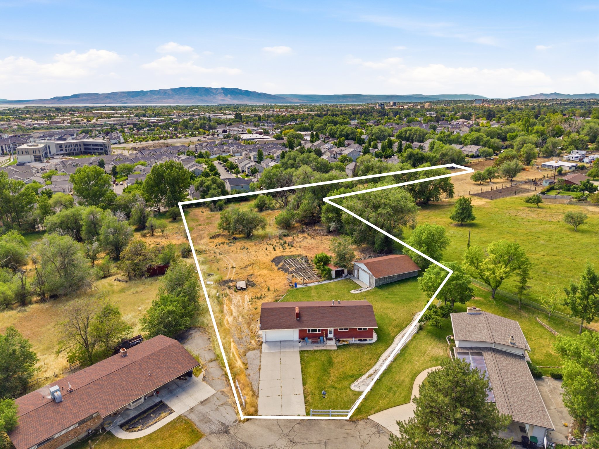 Expansive property featuring a red ranch-style home, a detached garage, and mature trees