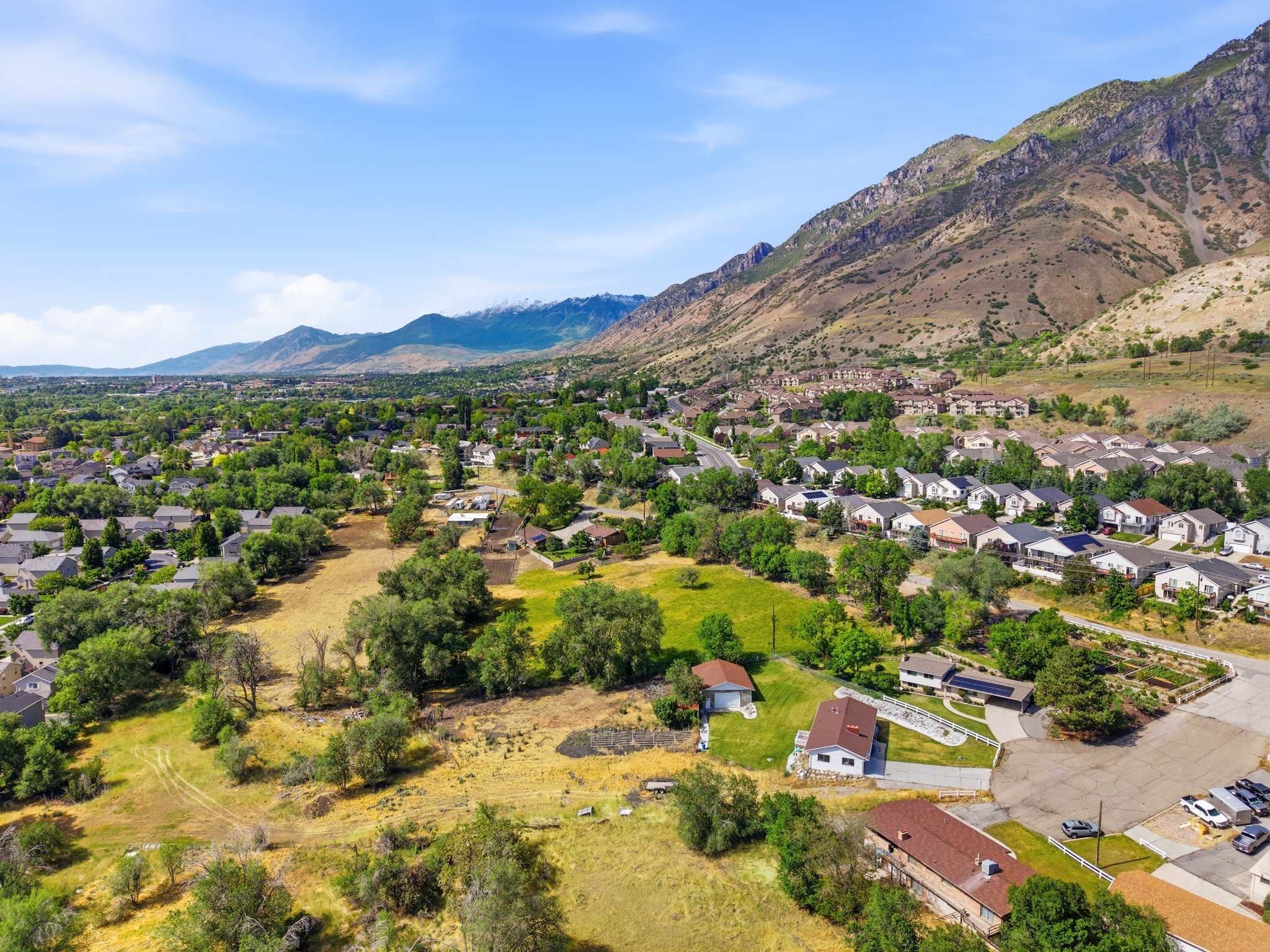 Expansive suburban landscape featuring a mountainous backdrop, scattered residential structures, and mature green trees