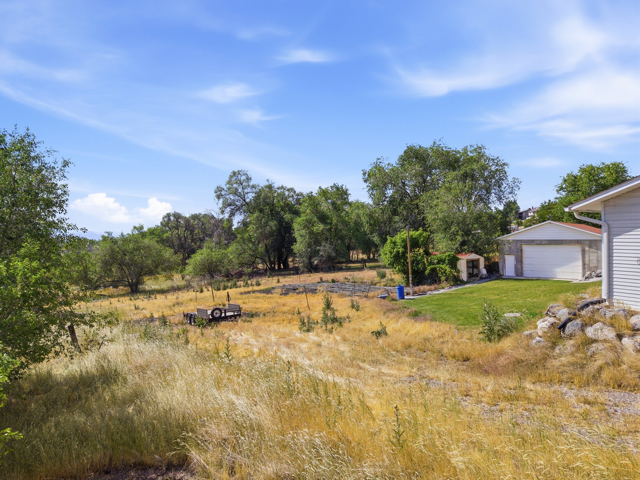 Expansive property featuring mature trees, a detached garage with a white roll-up door, a separate outbuilding, and a grassy lawn area