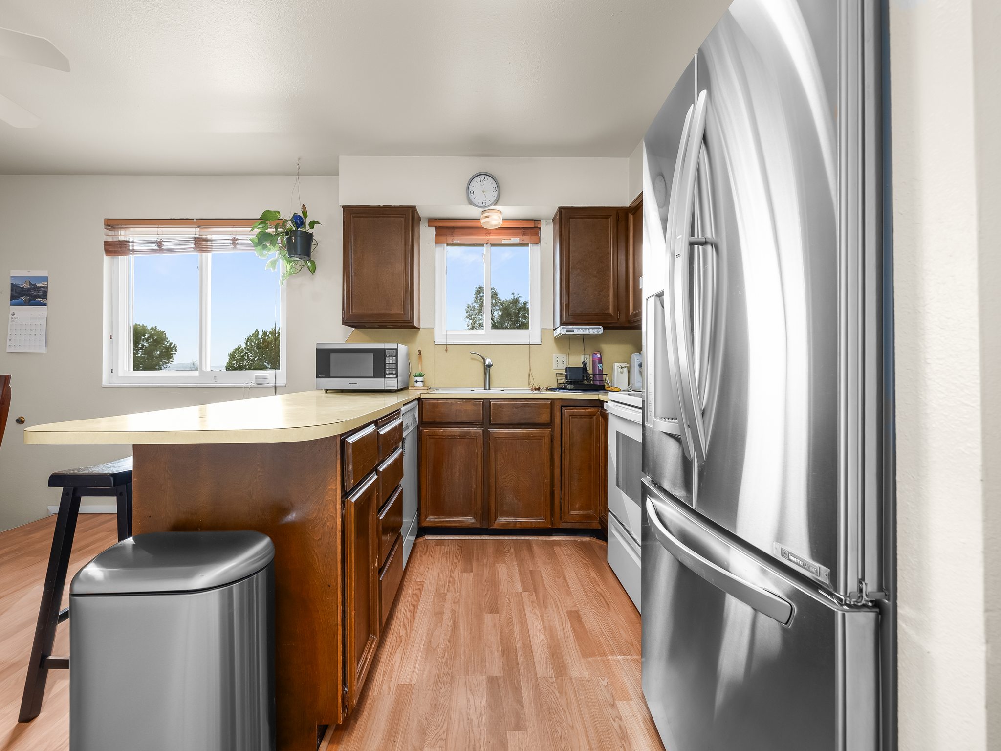 Open-concept kitchen featuring wood-finish flooring, dark wood cabinetry, light countertops, and a full suite of stainless steel appliances