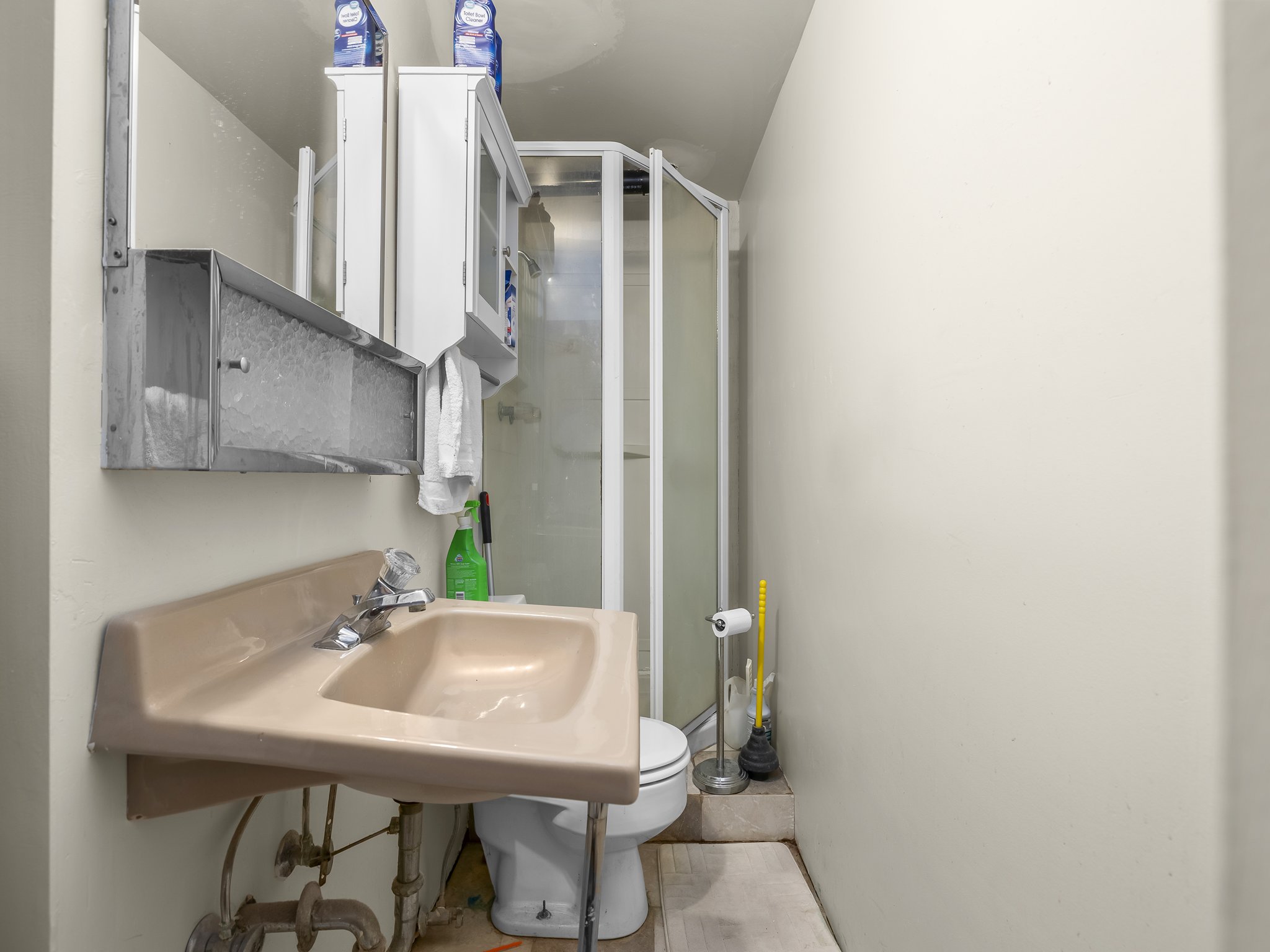 Compact bathroom featuring a corner shower enclosure, a wall-mounted sink with exposed plumbing, and a white medicine cabinet
