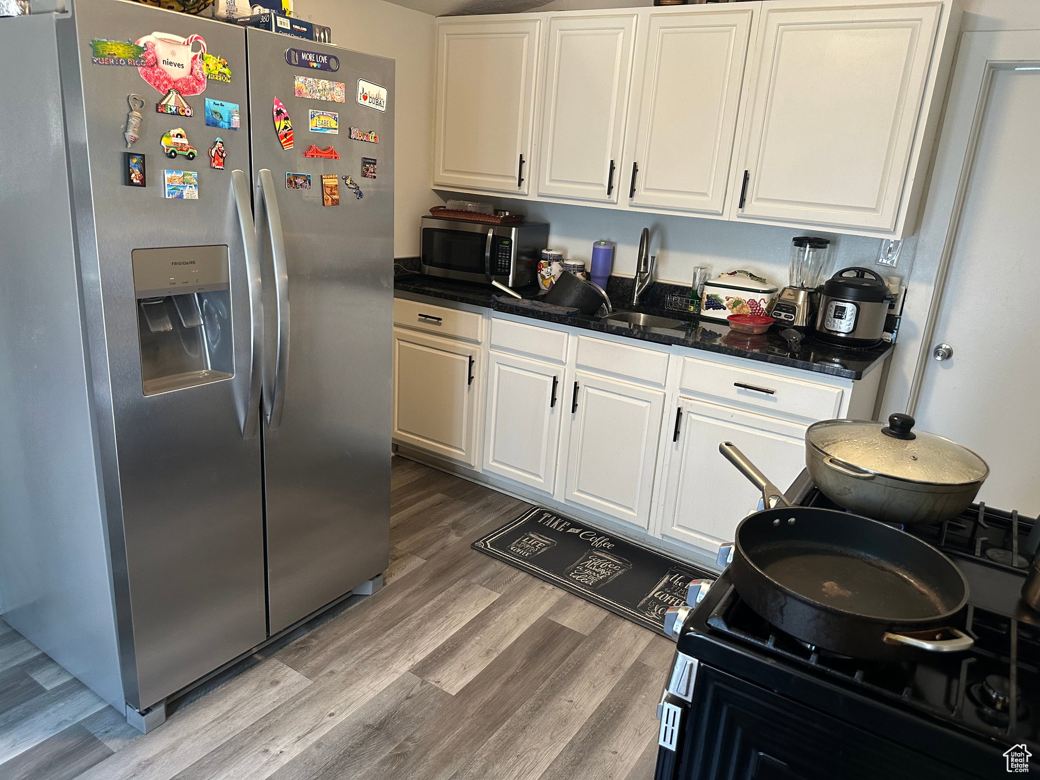 Kitchen featuring white cabinetry with dark hardware, a stainless steel side-by-side refrigerator, dark countertops, and wood-finish flooring