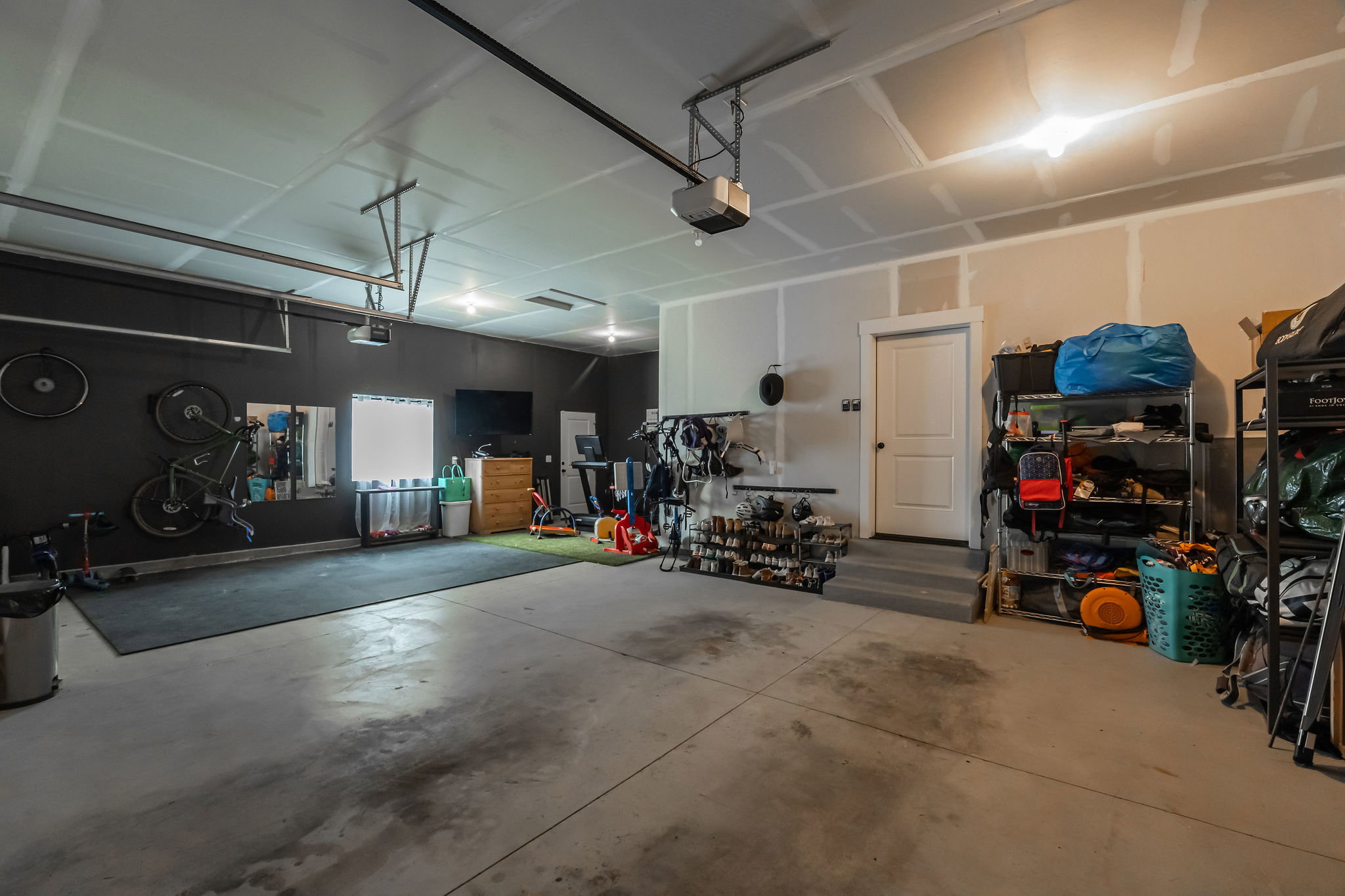 Spacious garage featuring concrete flooring, unpainted drywall, and a white interior door with steps