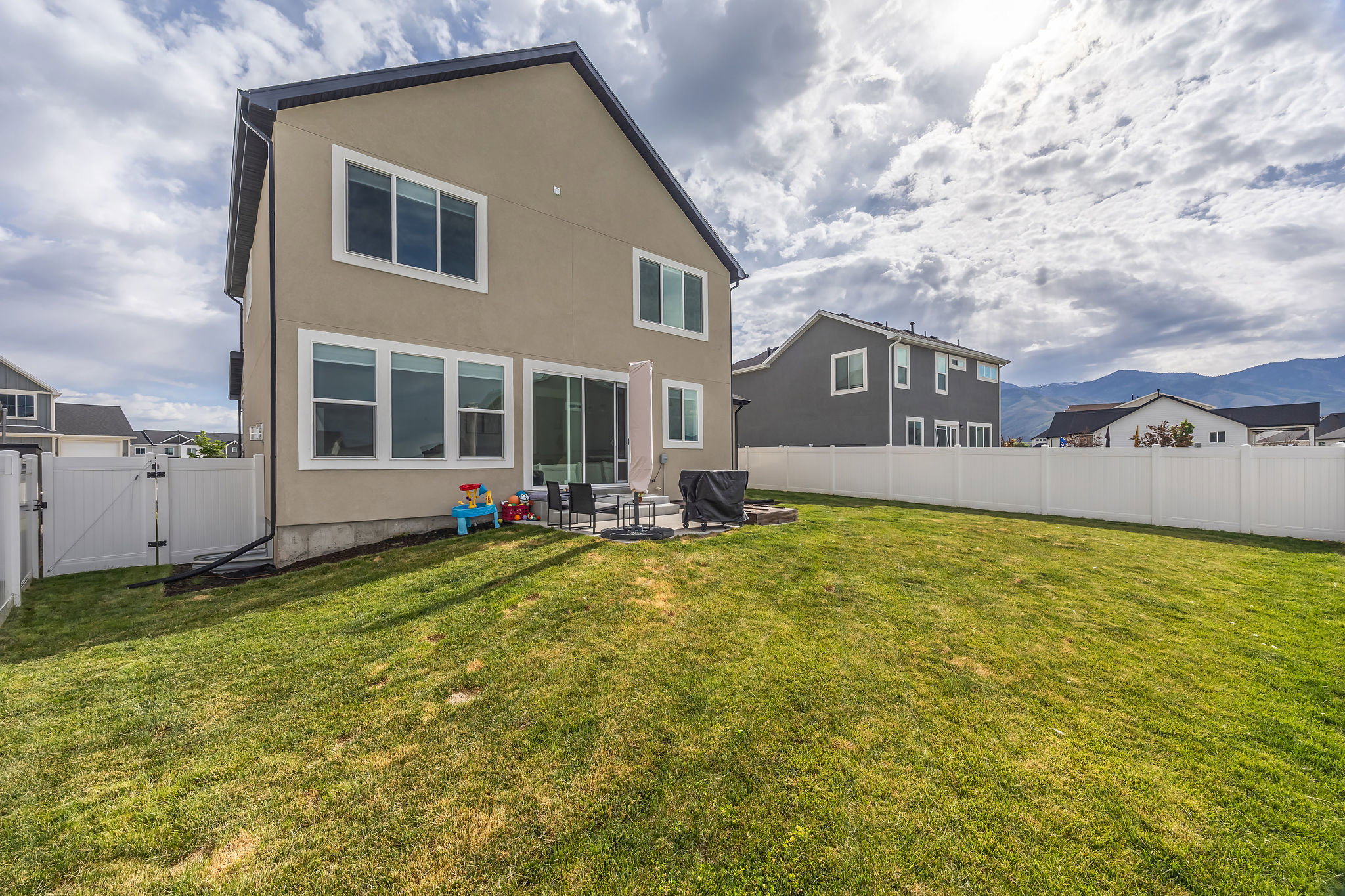 Expansive backyard featuring a manicured lawn, white vinyl fencing, and a concrete patio