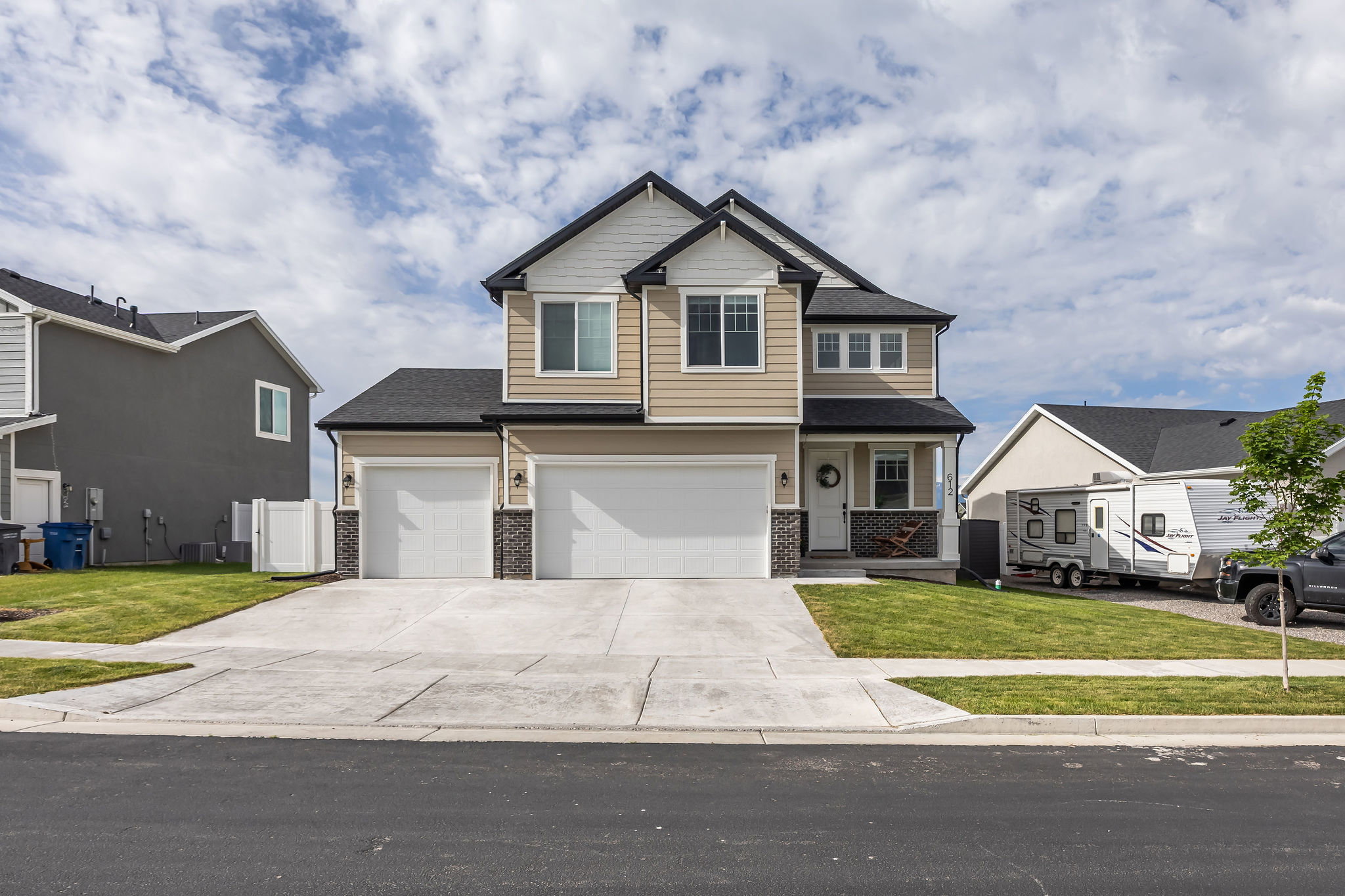 Two-story property featuring light tan horizontal siding, dark roof shingles, and a dual-door garage with brick accents