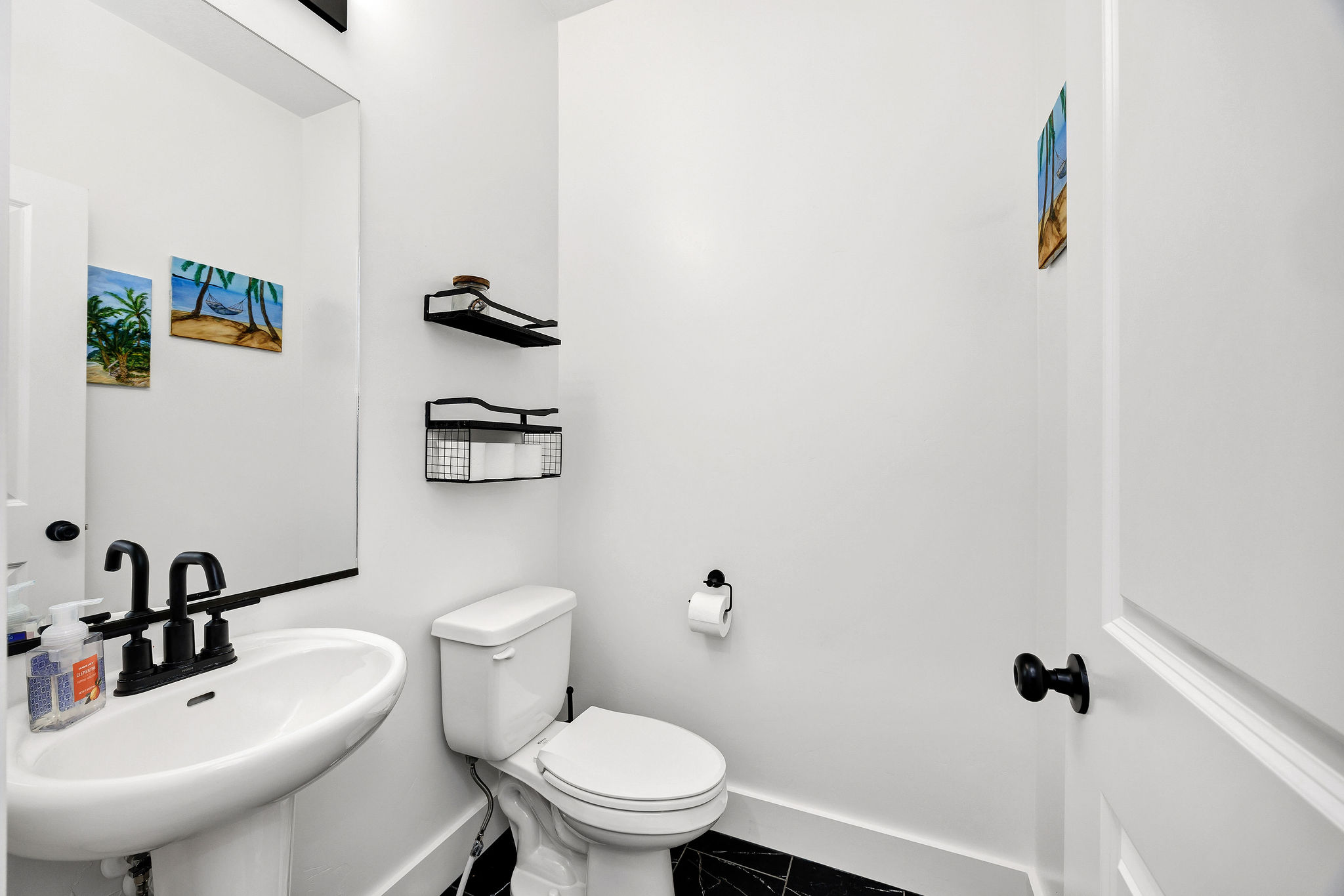 Pedestal sink with matte black faucet, wall-mounted mirror, and black and white floor tiles