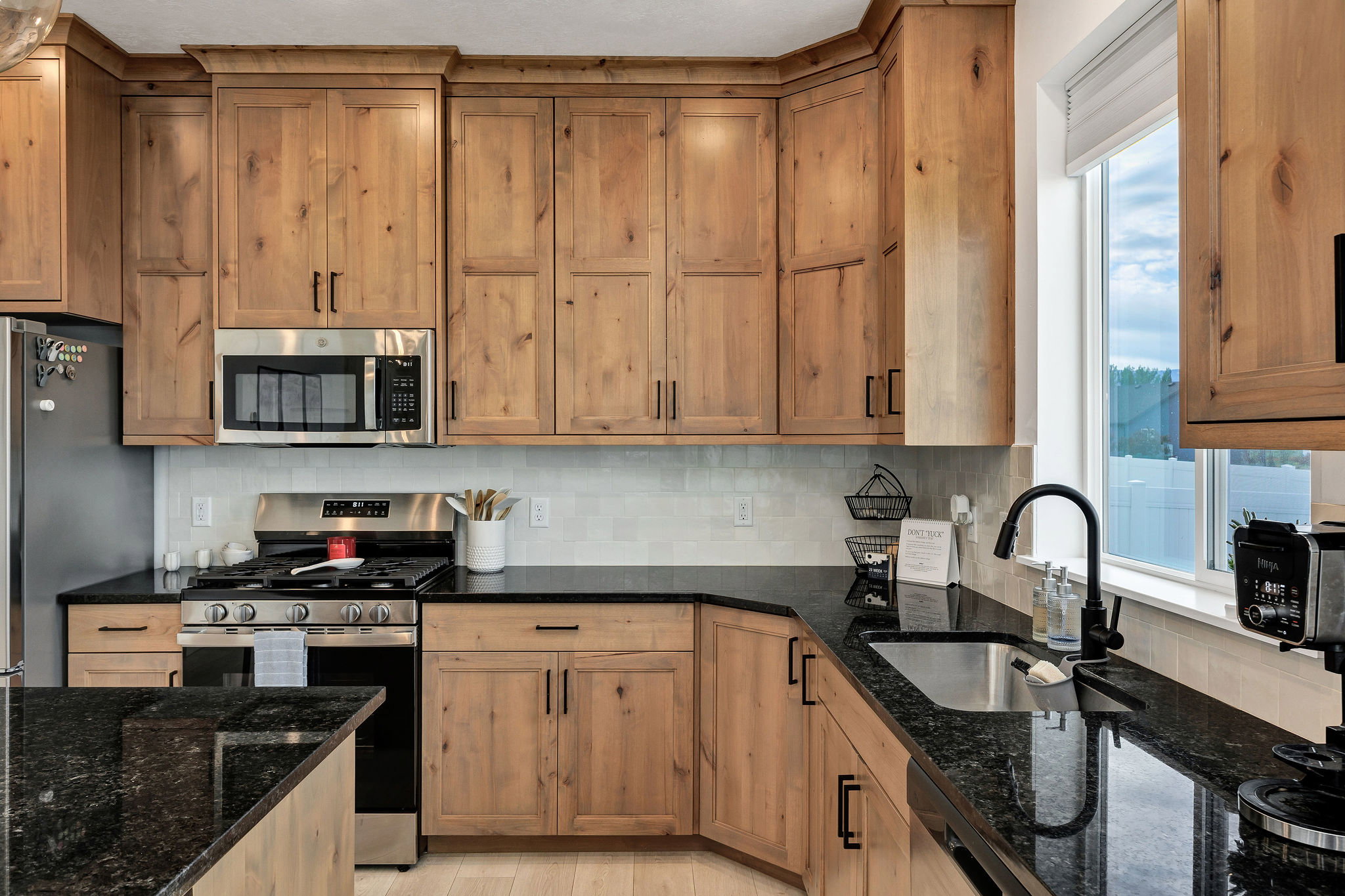 Kitchen featuring natural wood cabinetry, dark countertops, a stainless steel range, a built-in microwave, and a single-basin sink with a matte black faucet