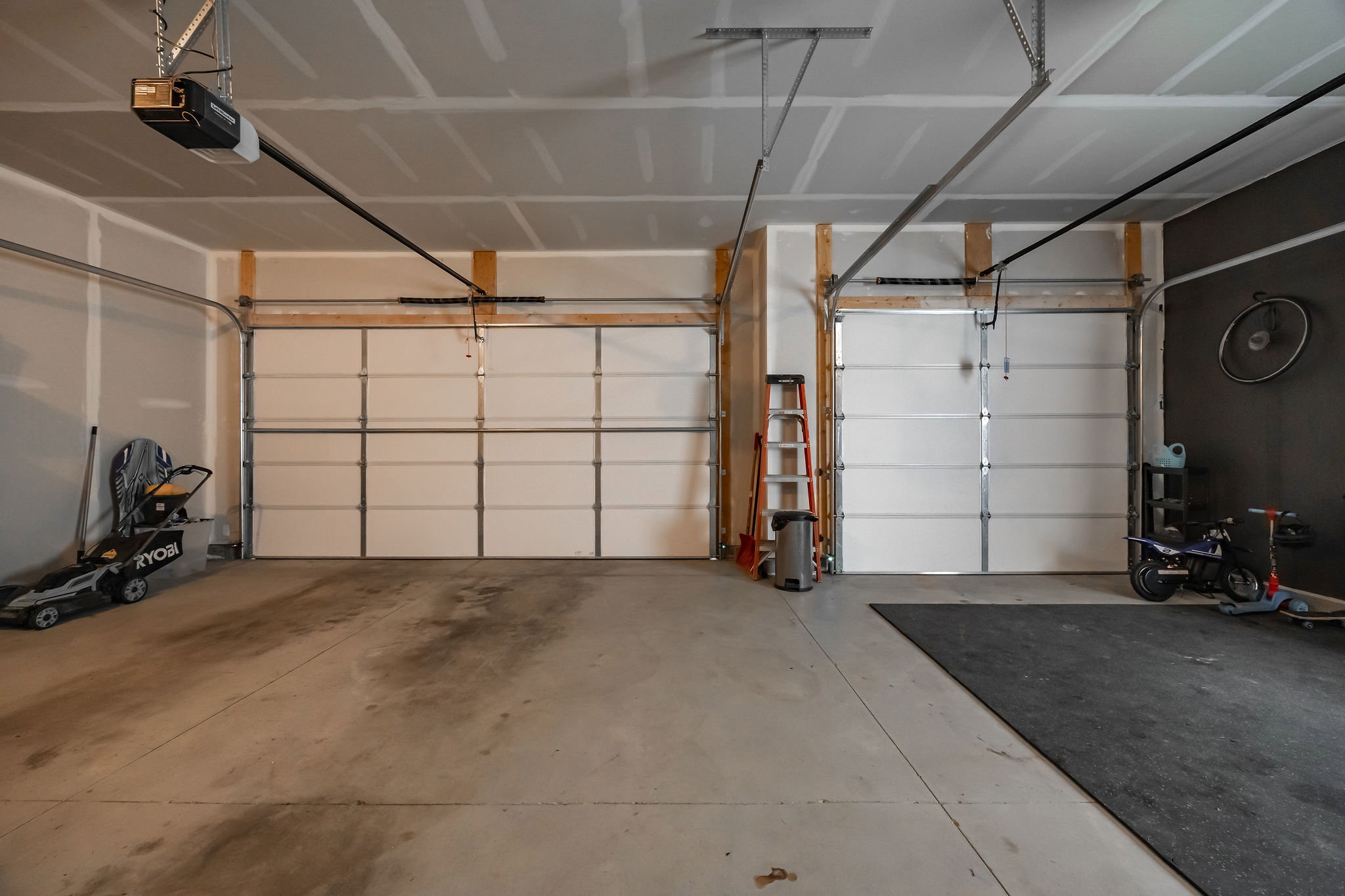 Spacious two-car garage featuring concrete flooring, two white panel garage doors, and exposed ceiling joists