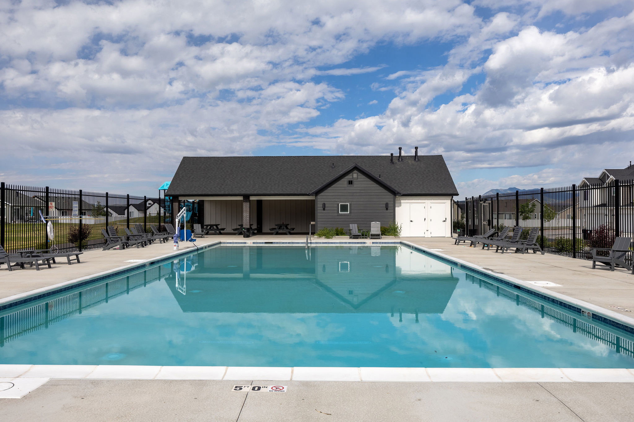 Community swimming pool with a concrete surround, dark metal perimeter fencing, and a dedicated pool house