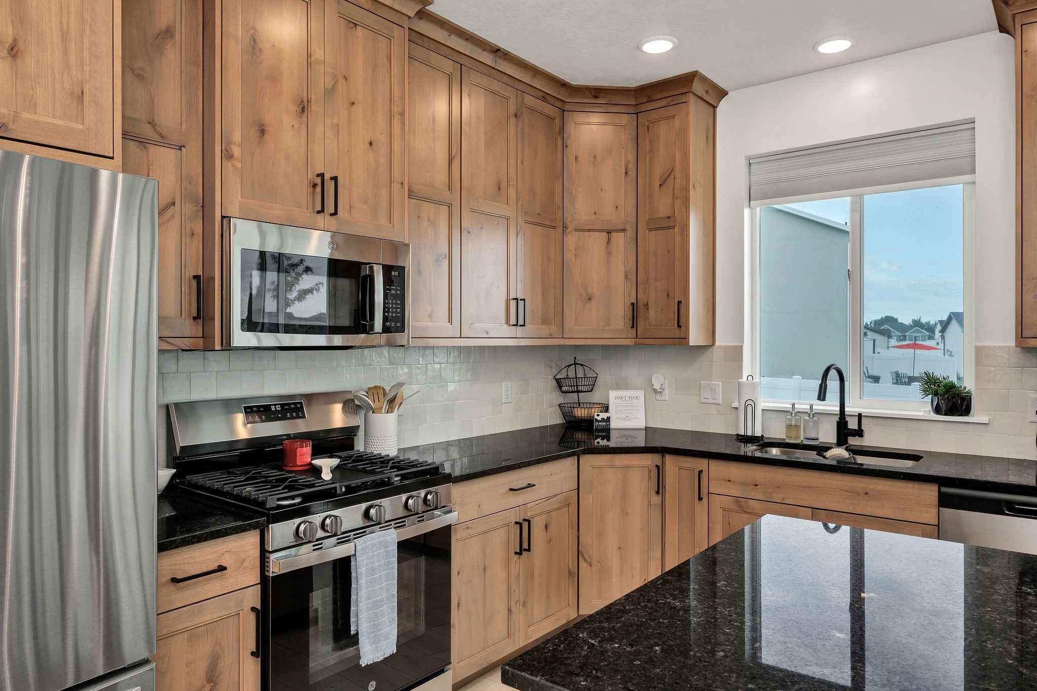 Kitchen featuring knotty wood cabinetry, black countertops, stainless steel appliances, a subway tile backsplash, and a sink with a black gooseneck faucet