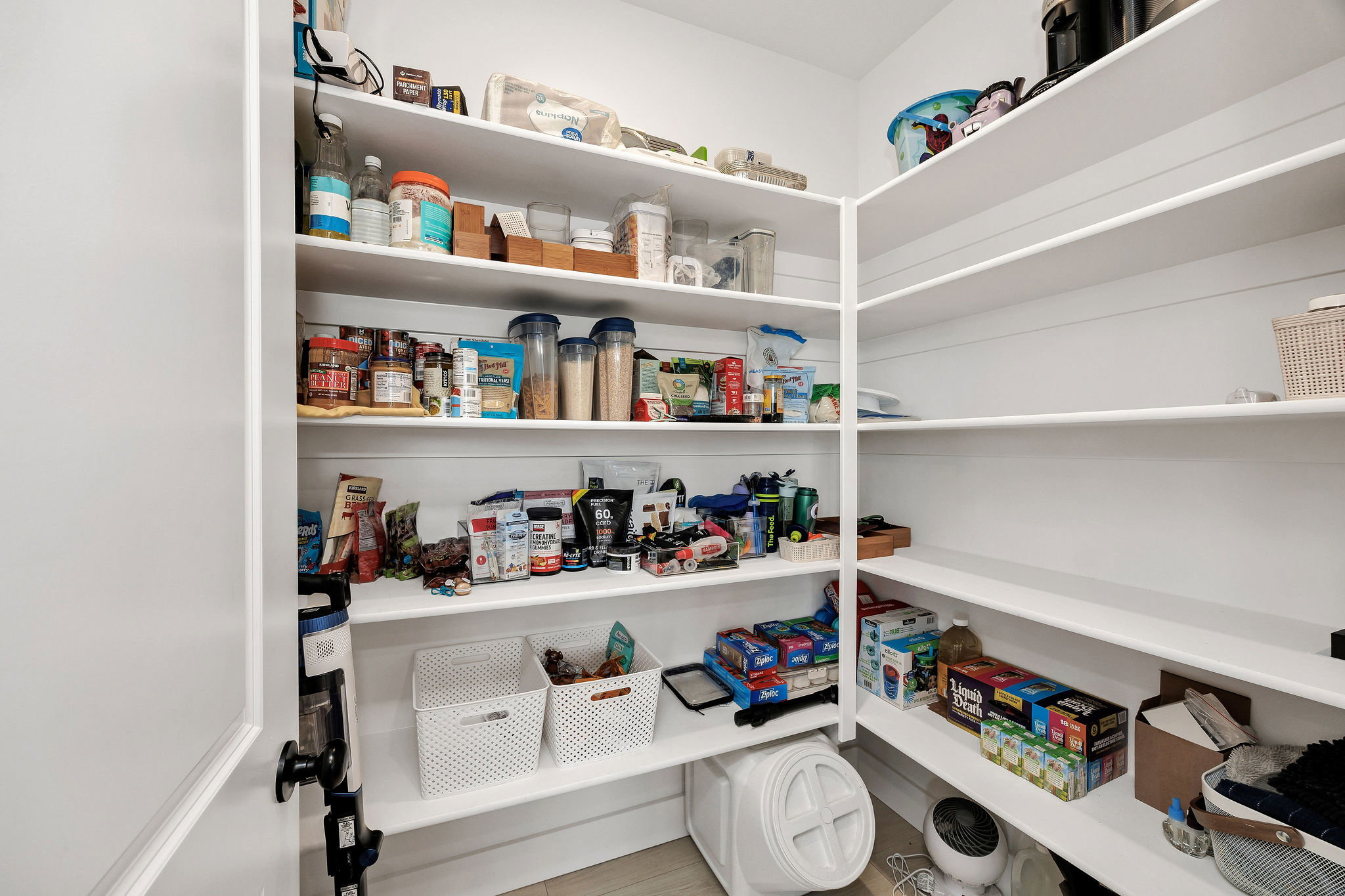 Spacious walk-in pantry featuring extensive built-in shelving, white painted walls, and light-toned flooring