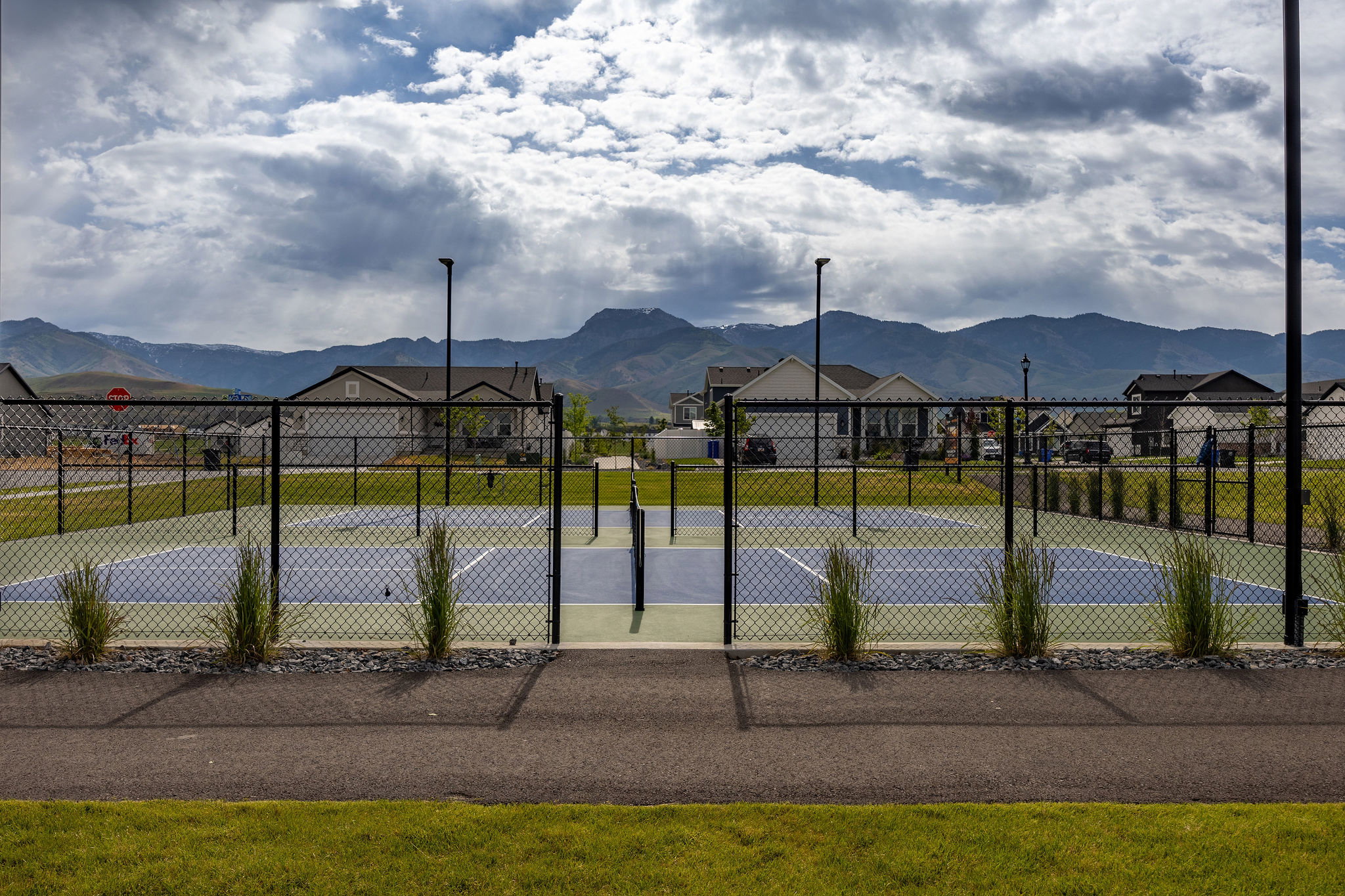 Fenced recreational courts featuring a multi-sport surface with blue and green court lines, surrounded by landscape rock and ornamental grasses
