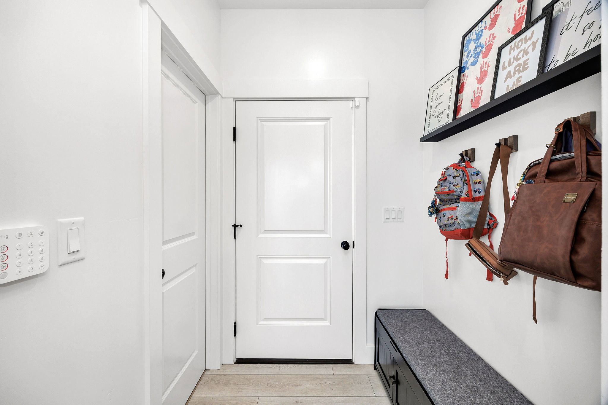 Entryway featuring light wood-finish flooring, white paneled doors with dark hardware, a built-in wall shelf, and a wall-mounted security system control panel