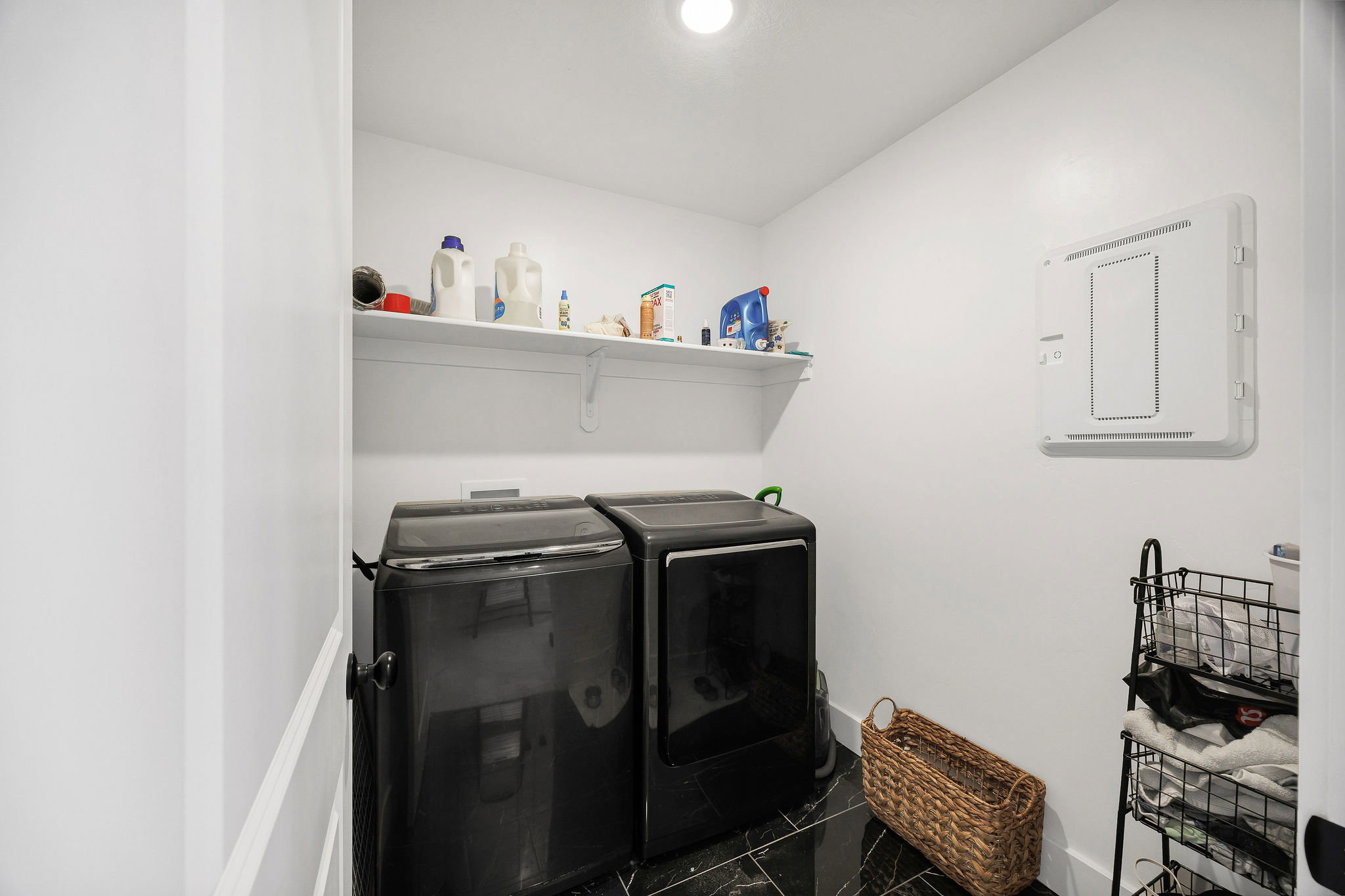Laundry area featuring black tile flooring, white walls, and an overhead shelf